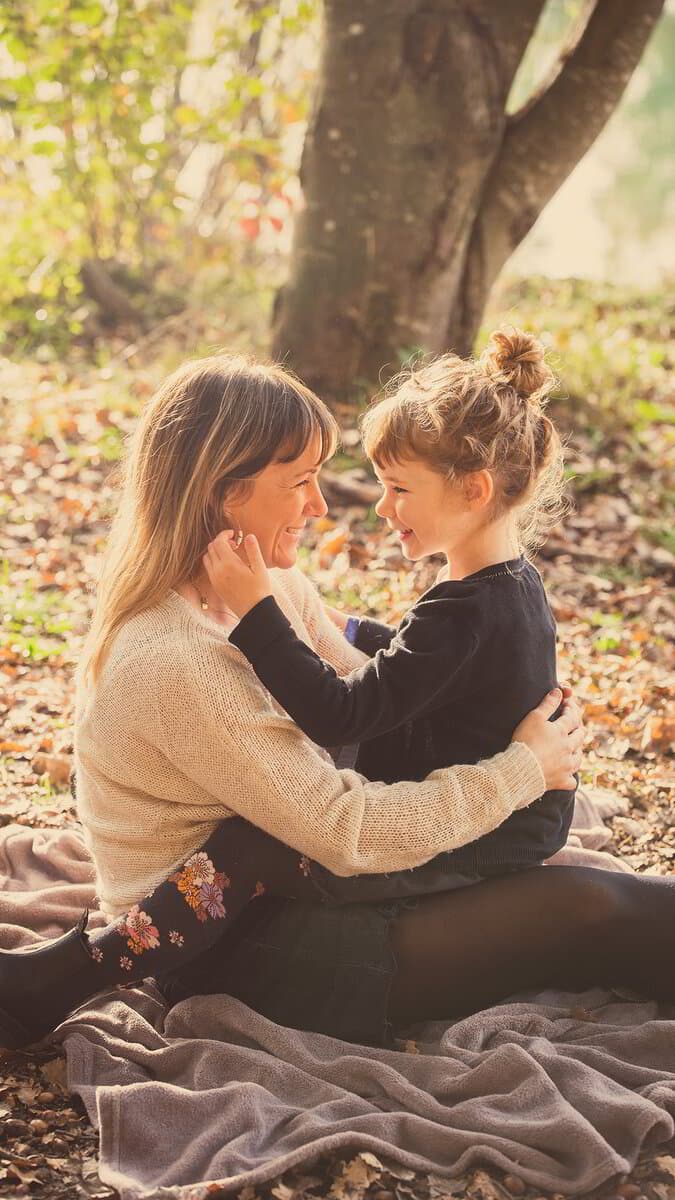 Une maman et sa fille assises sur une couverture parmi les feuilles d’automne