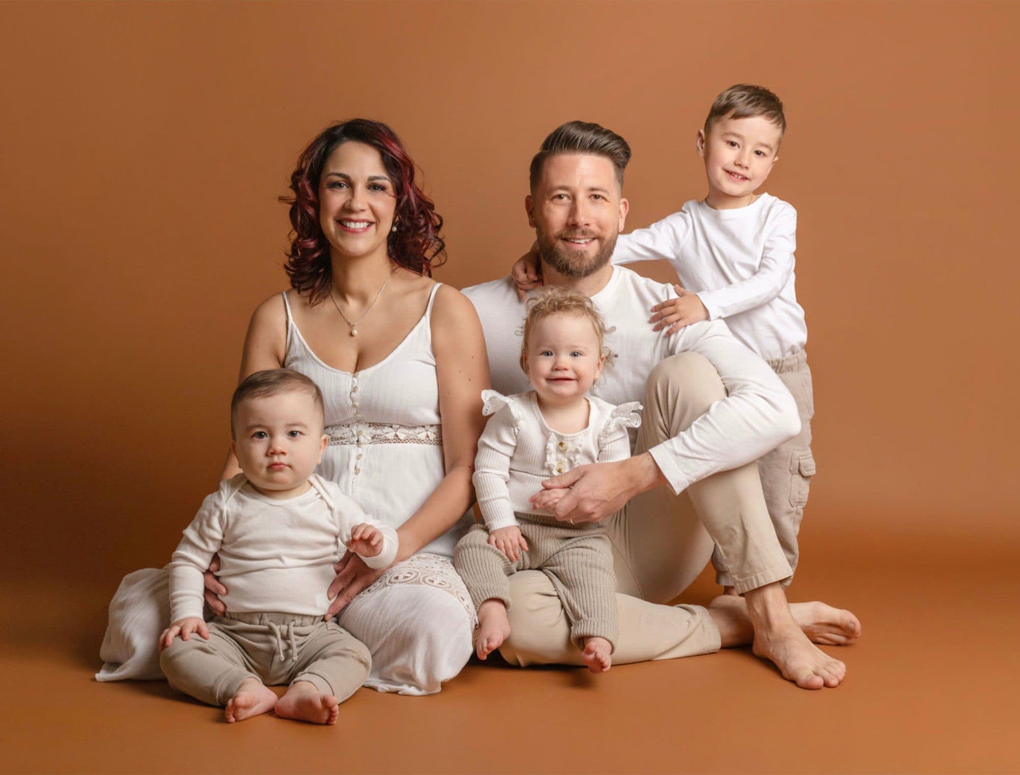 Une famille et ses trois jeunes enfants assis au studio sur un fond orange, en blanc et beige