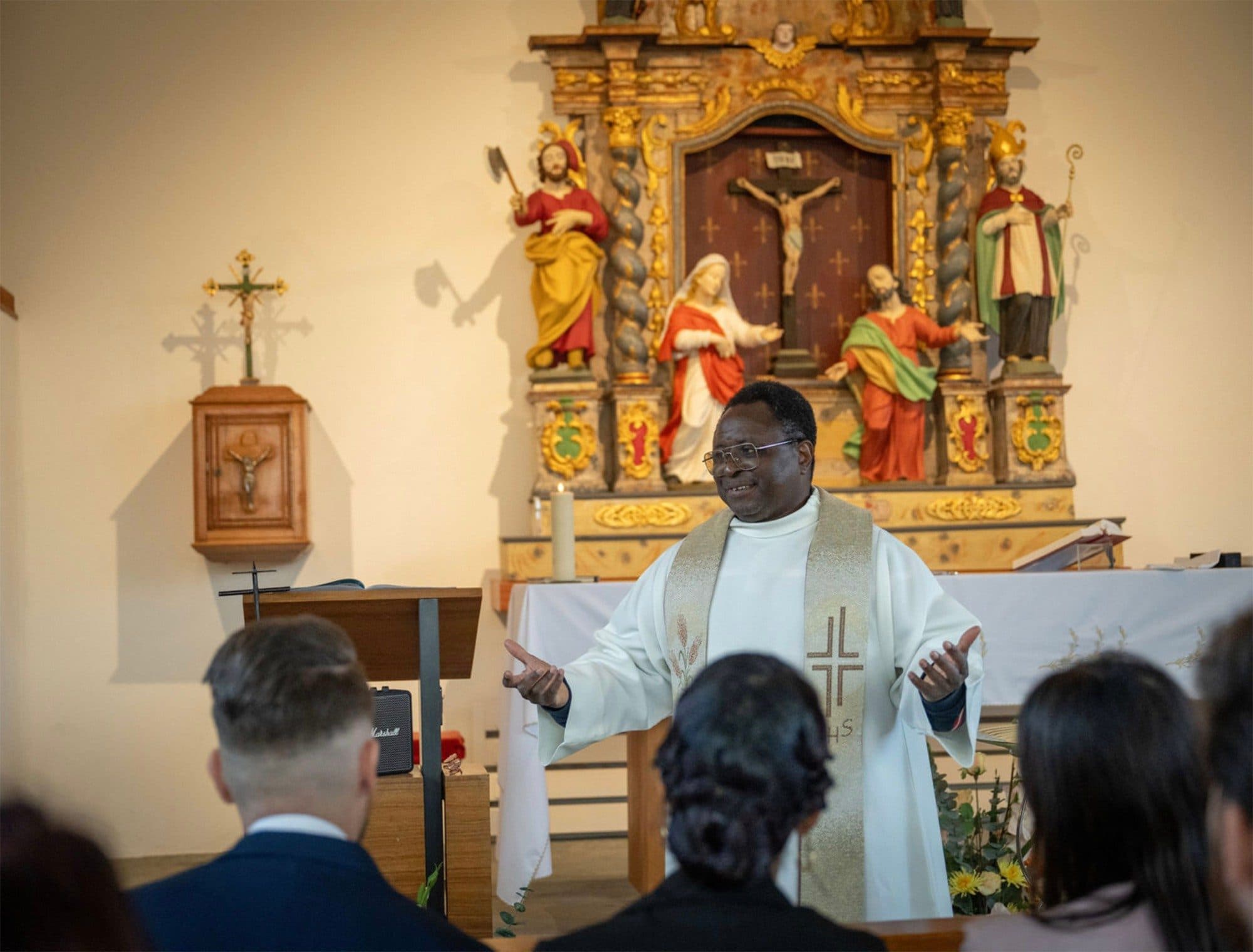 Le prêtre parle devant l’autel doré d’une église, la famille assise au premier rang