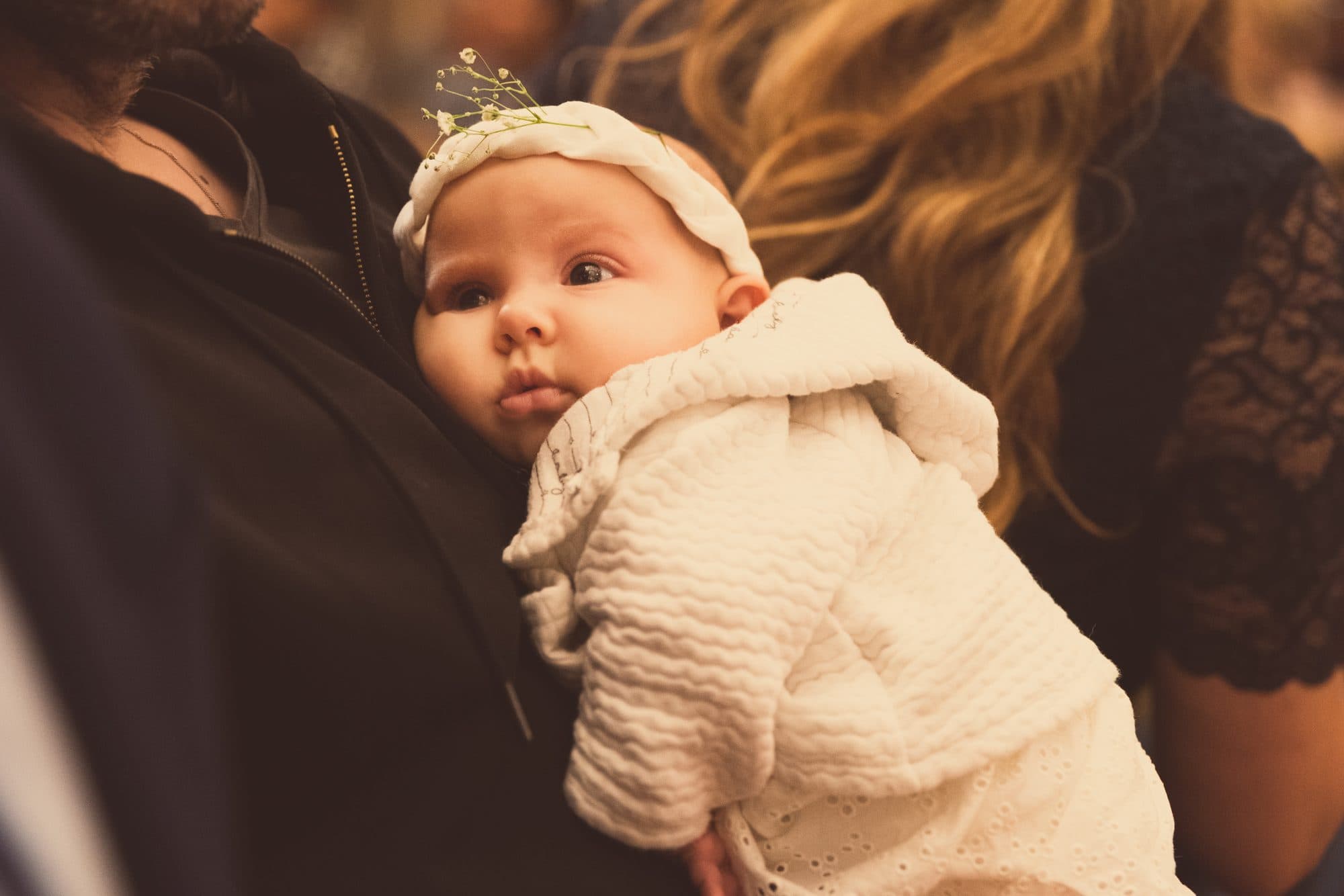 Un bébé coiffé d’une petite couronne regarde par-dessus l’épaule de sa maman