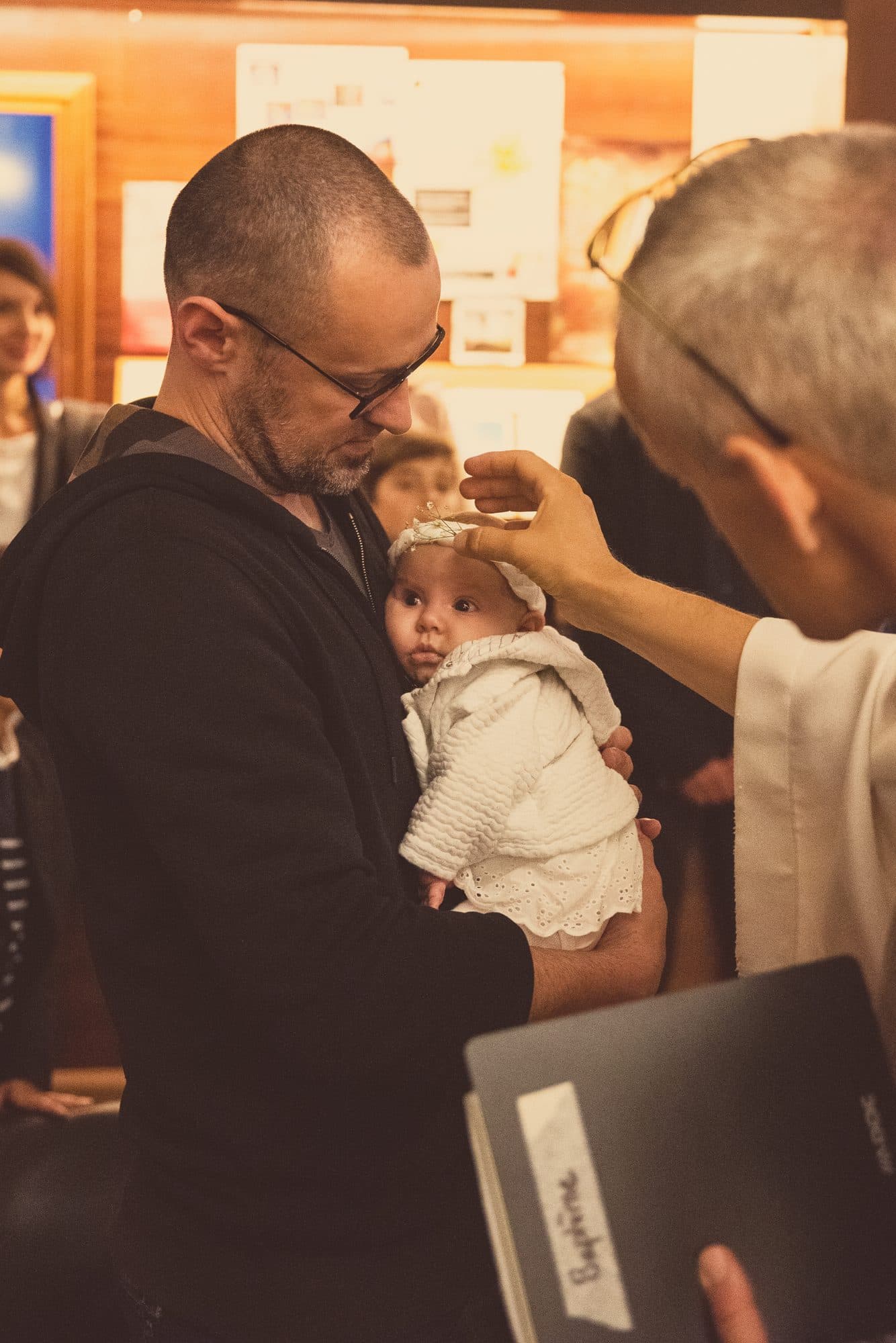 Le prêtre trace un signe sur le front d’un bébé tenu par son papa