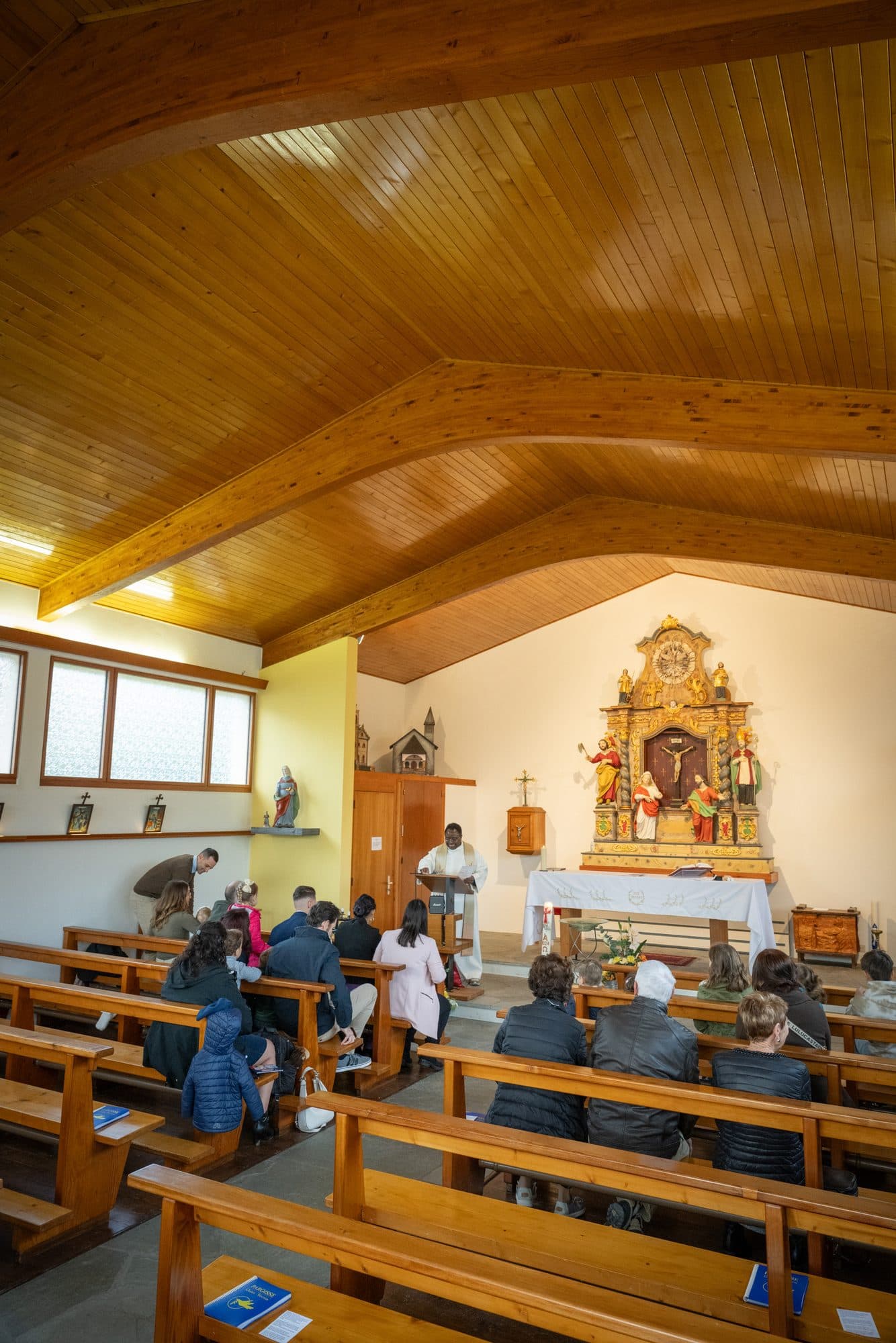 Une église au plafond de bois, la famille réunie dans les bancs devant l’autel doré