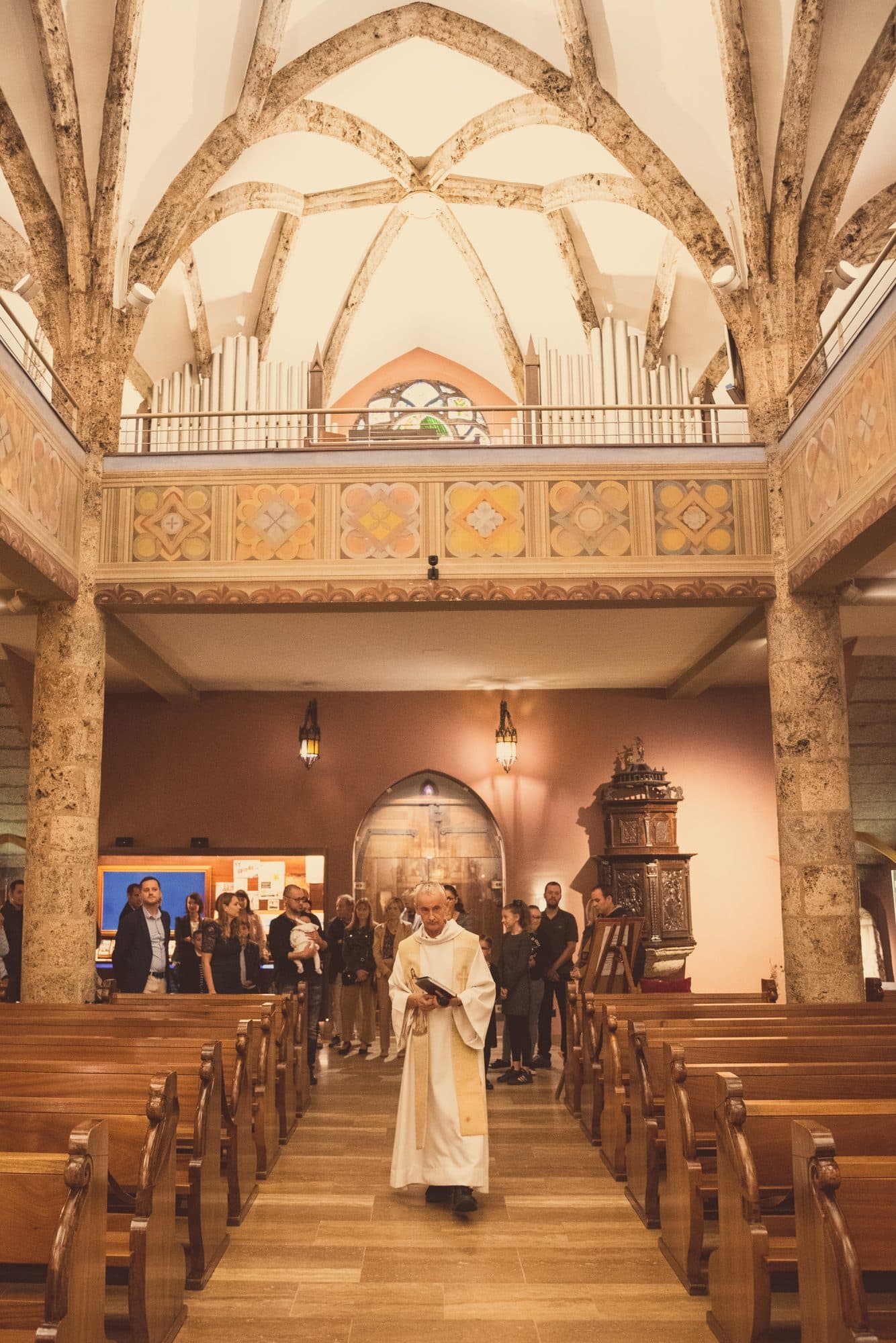 Le prêtre remonte l’allée d’une église aux voûtes peintes, entre les bancs