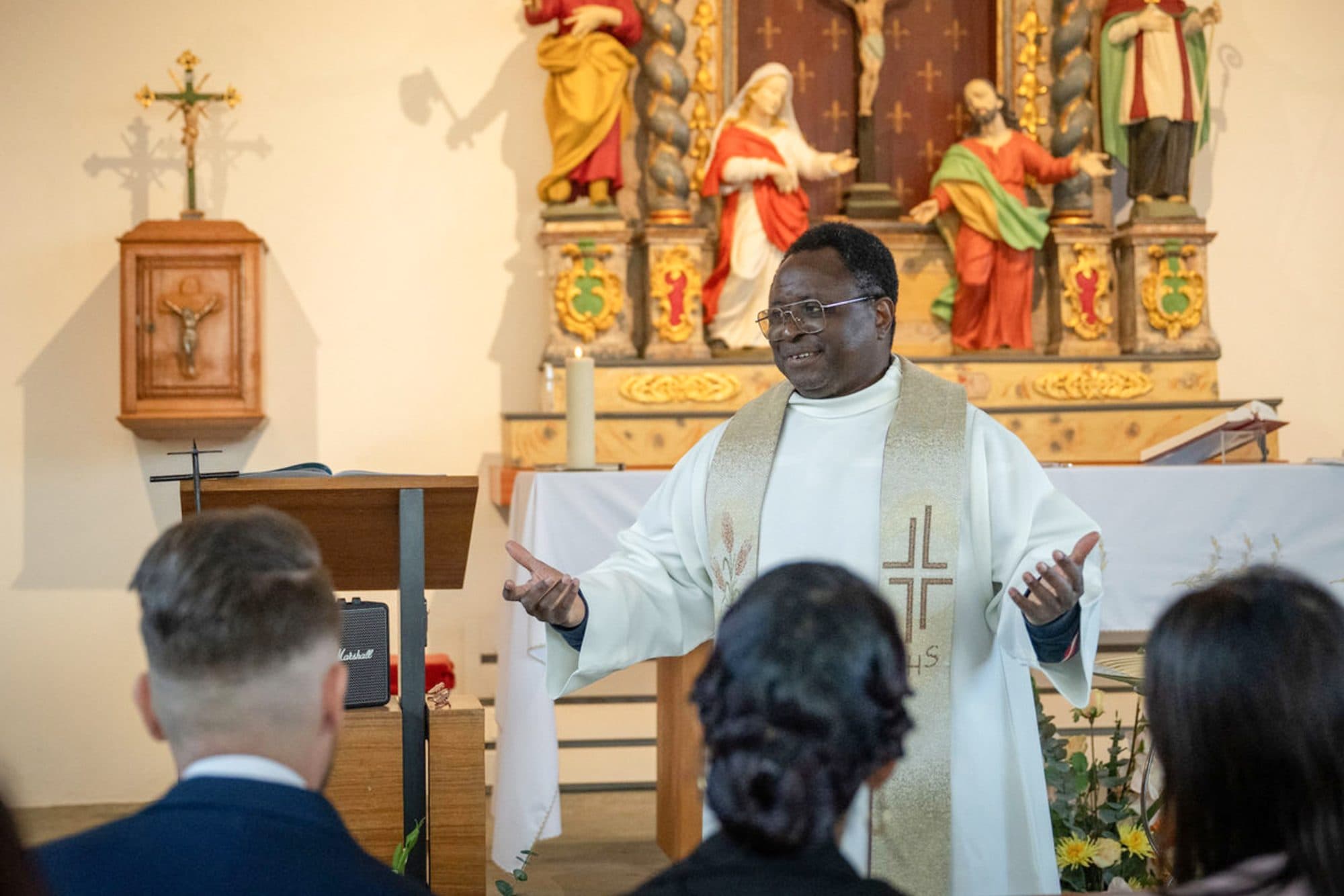 Le prêtre parle devant l’autel doré d’une église, la famille assise au premier rang