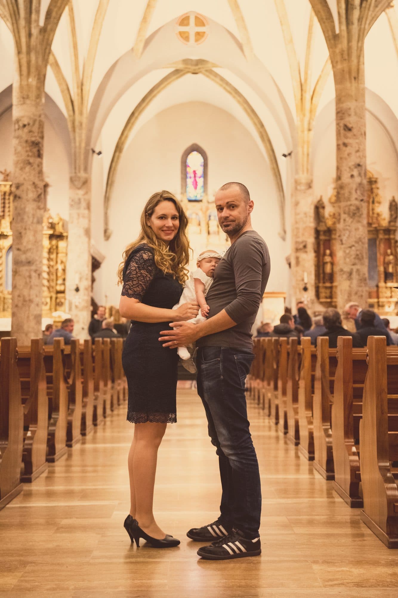 Les parents posent avec leur bébé dans l’allée d’une église aux voûtes blanches