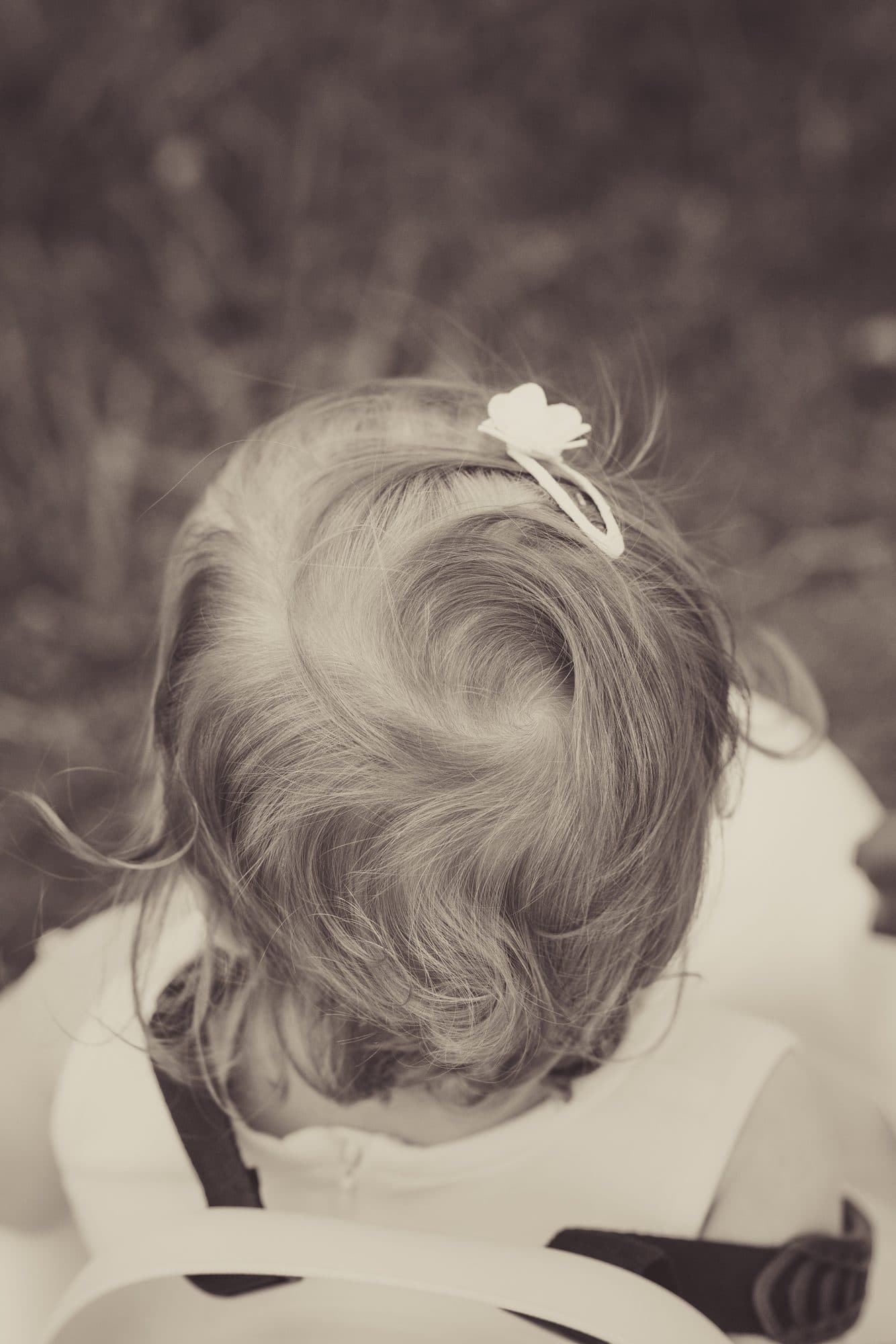 Une petite fille vue de dos, une barrette fleurie dans les cheveux, en tons sépia