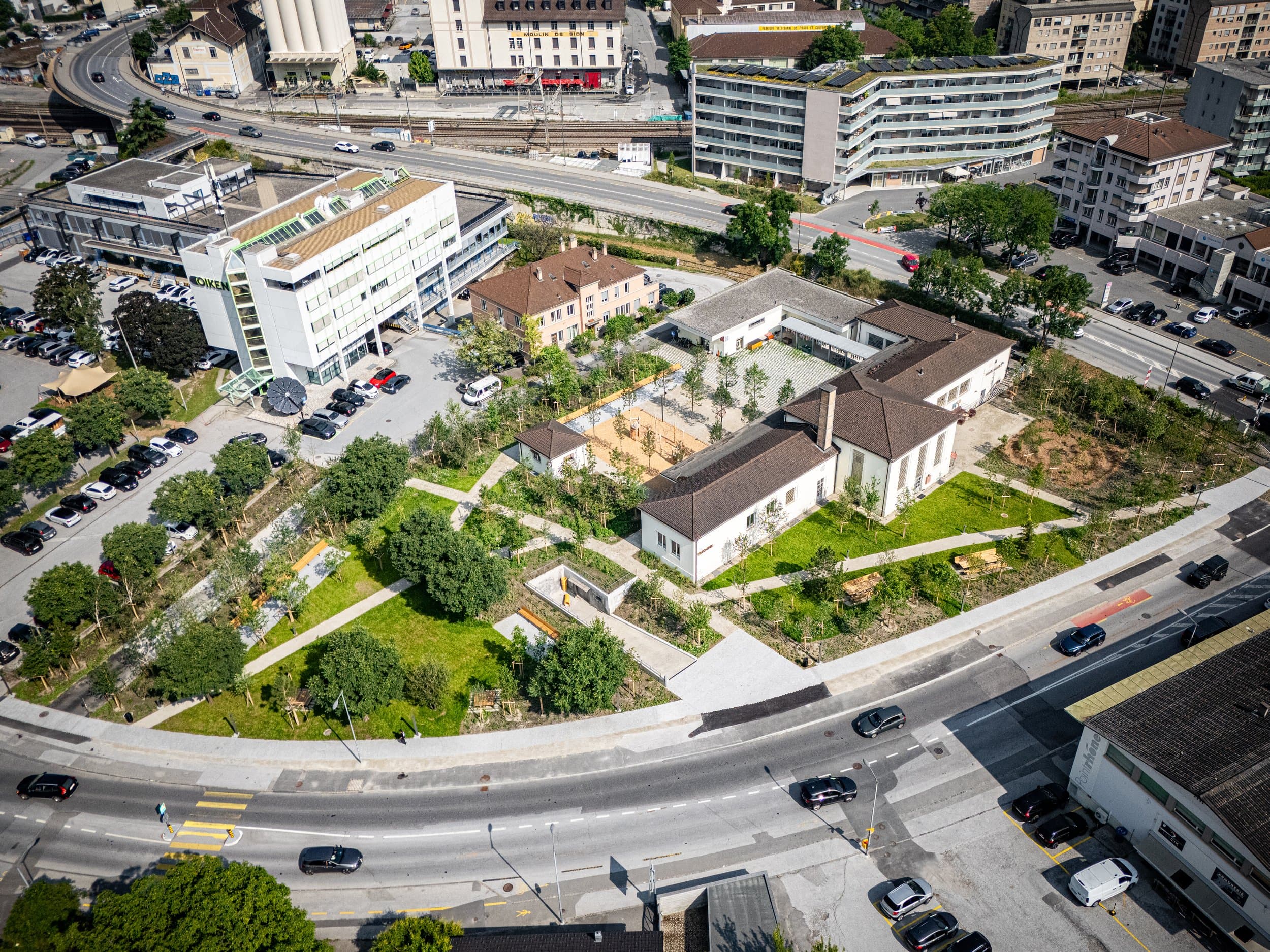 Vue au drone de L’Archipel à Sion, ses bâtiments et son jardin public entourés de routes et d’immeubles, photo d’architecture