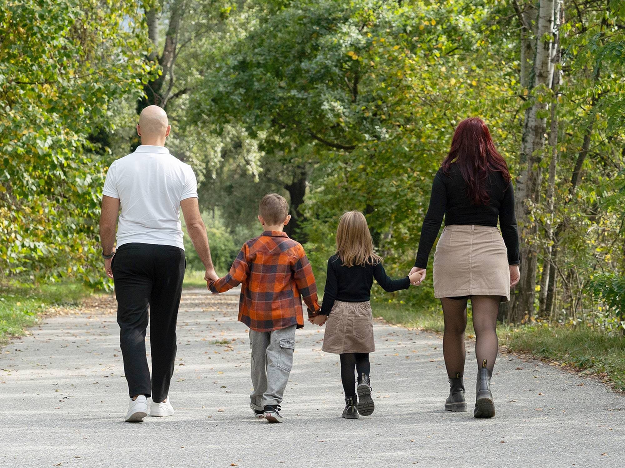 Des parents et leurs deux enfants marchent main dans la main sur un chemin bordé d’arbres