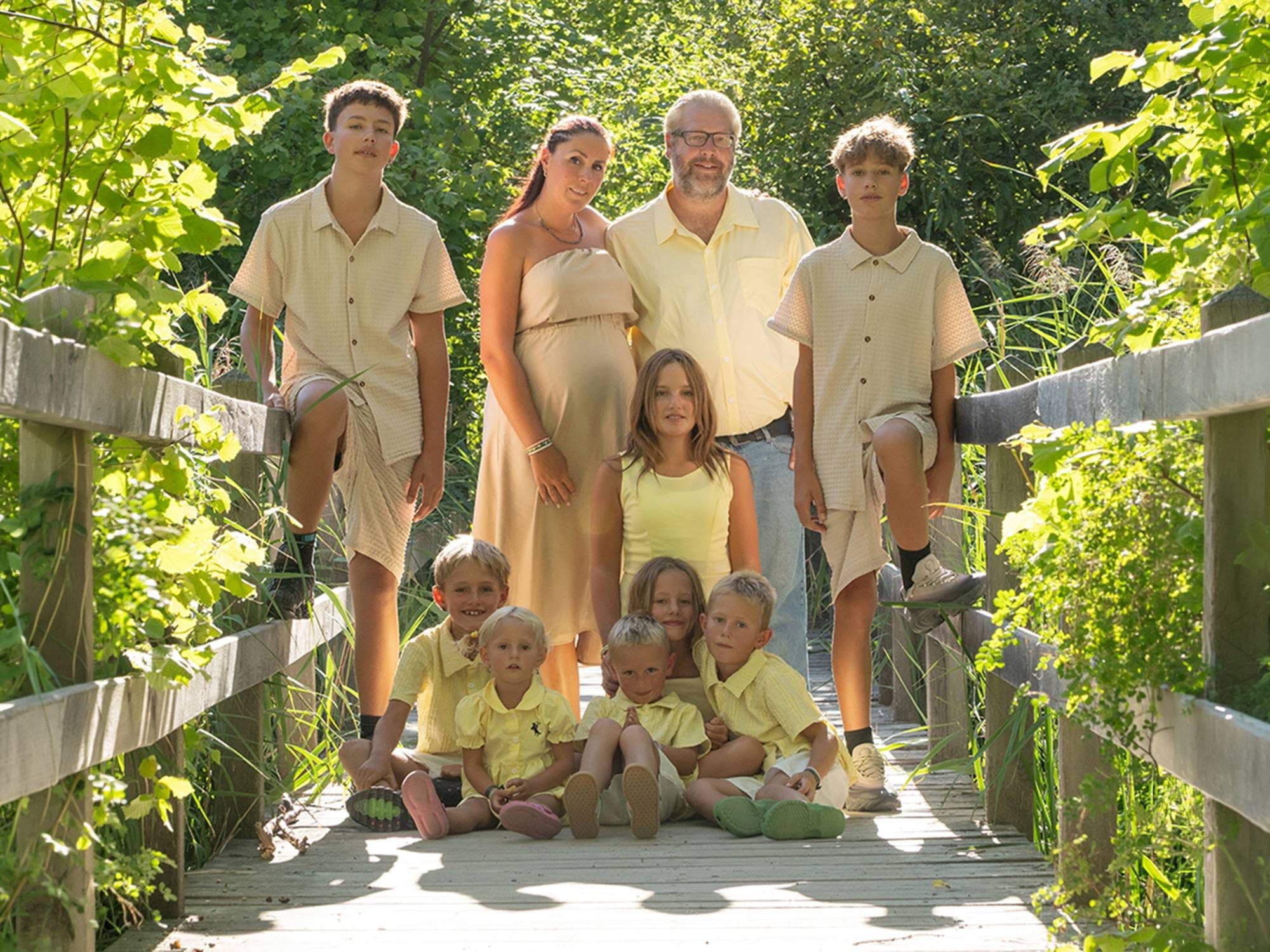 Une grande famille habillée de jaune et de beige, réunie sur une passerelle en bois dans la verdure