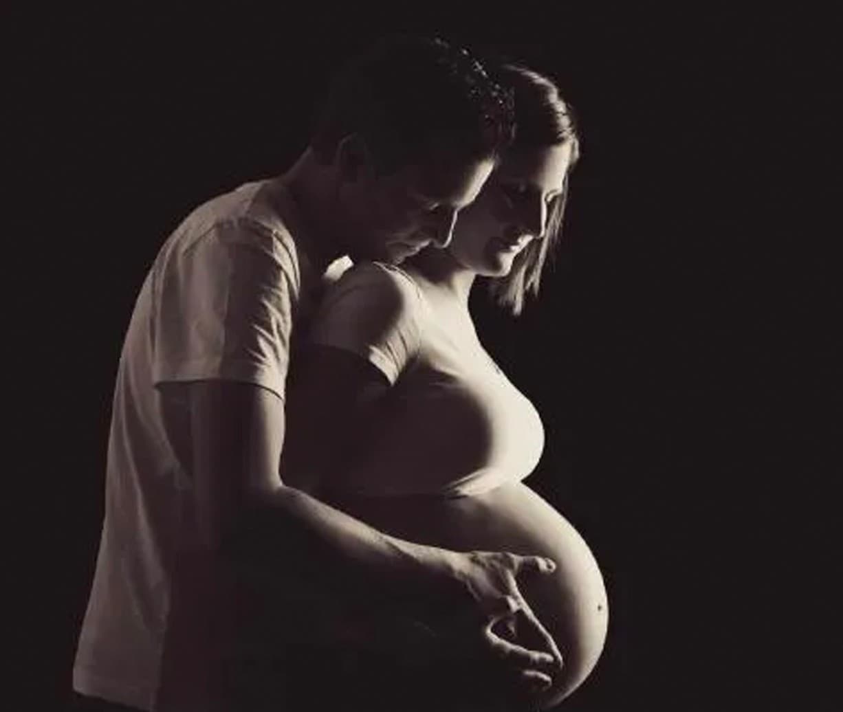 Des futurs parents en clair-obscur, les mains sur le ventre
