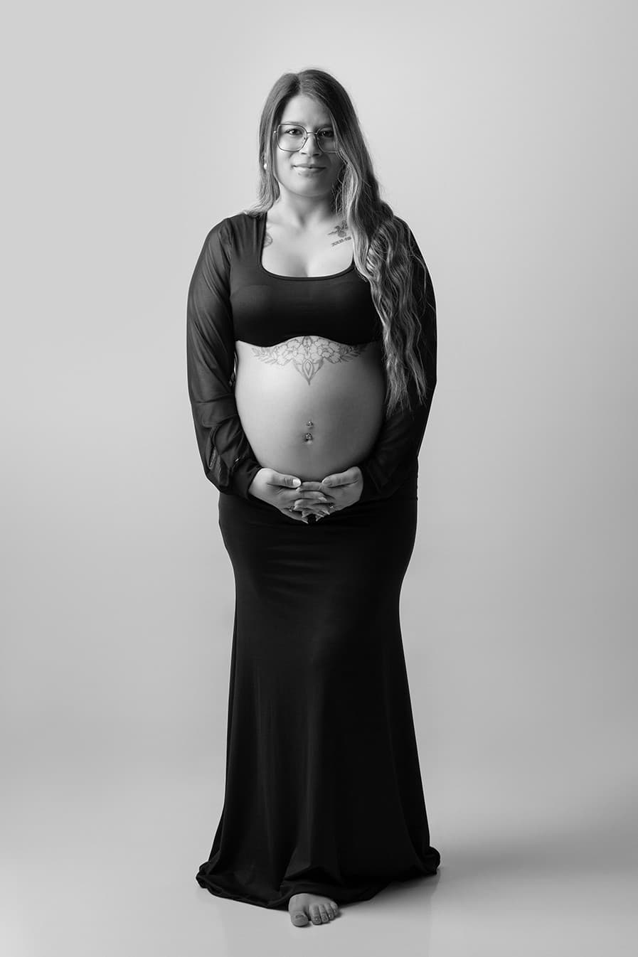 Future maman en haut court et longue jupe noire, les mains sur le ventre, en noir et blanc