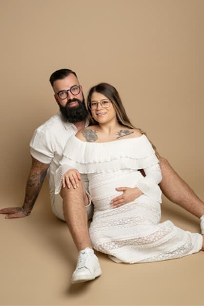 Future maman en robe blanche en dentelle assise près de son conjoint, fond beige