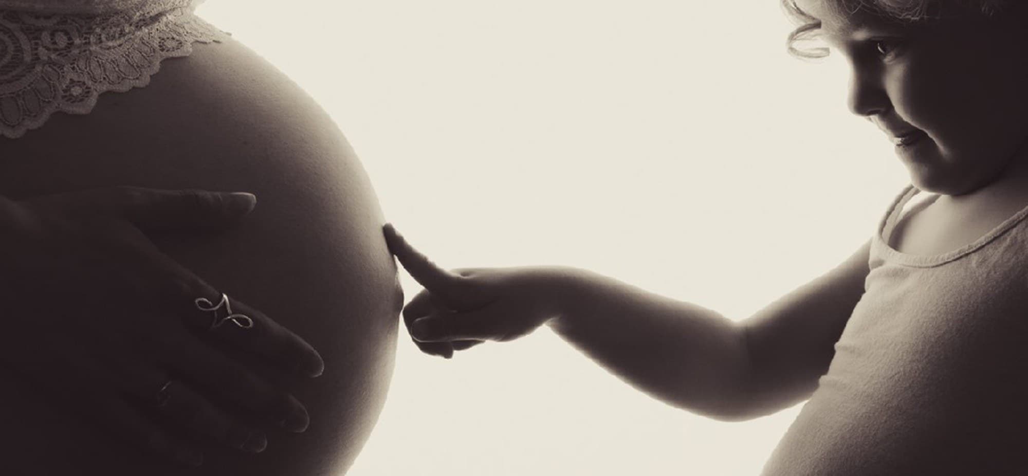 Silhouette d’un ventre rond au studio, un enfant le touche du bout du doigt, en tons sépia