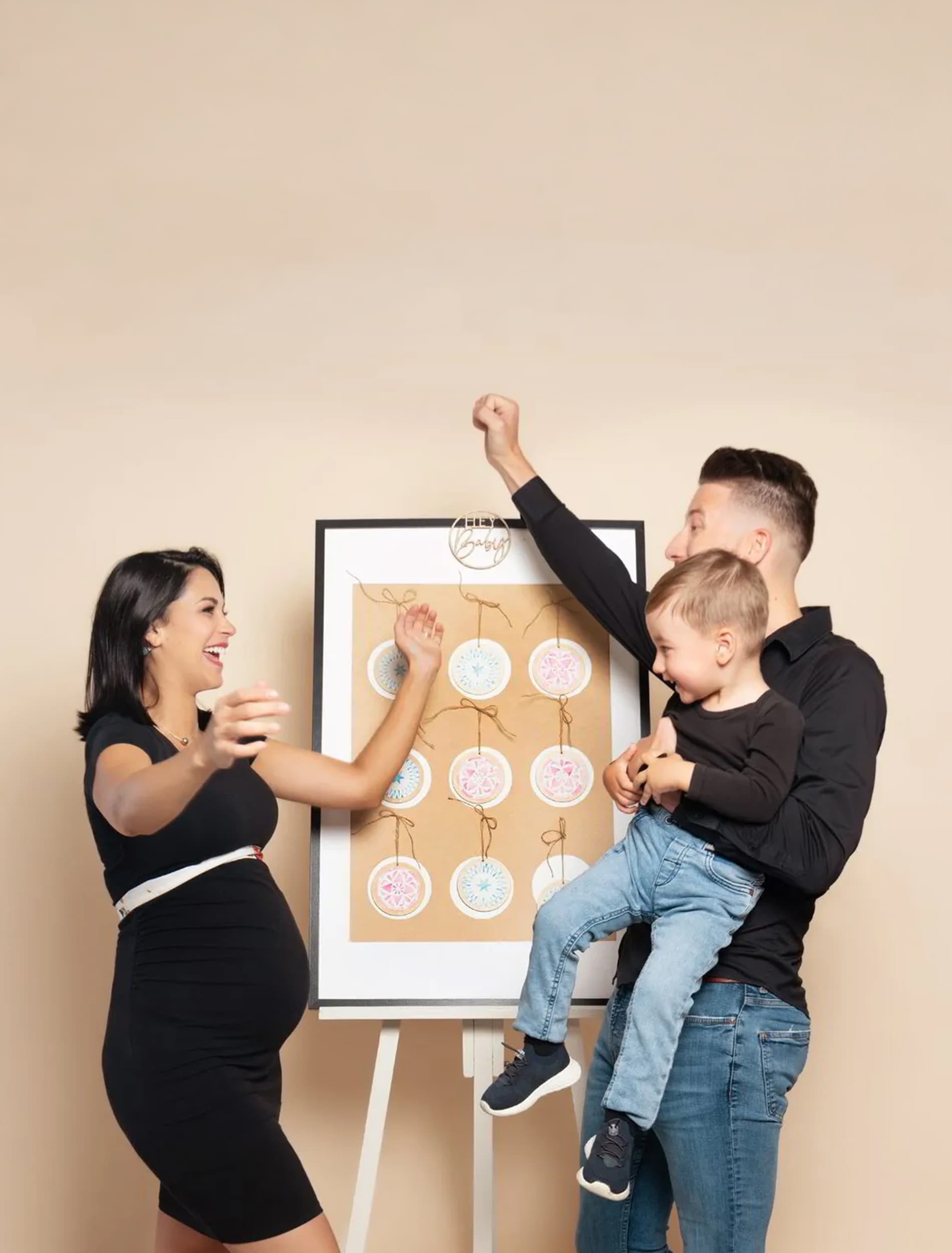 Une future maman éclate de joie face à son conjoint et à leur petit garçon, devant le tableau de la révélation