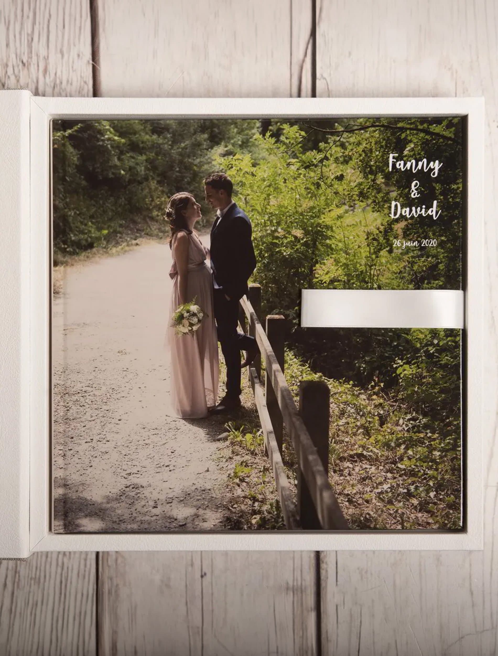 Un album de mariage dans son coffret blanc, la photo des mariés sur la couverture, sur un plancher en bois