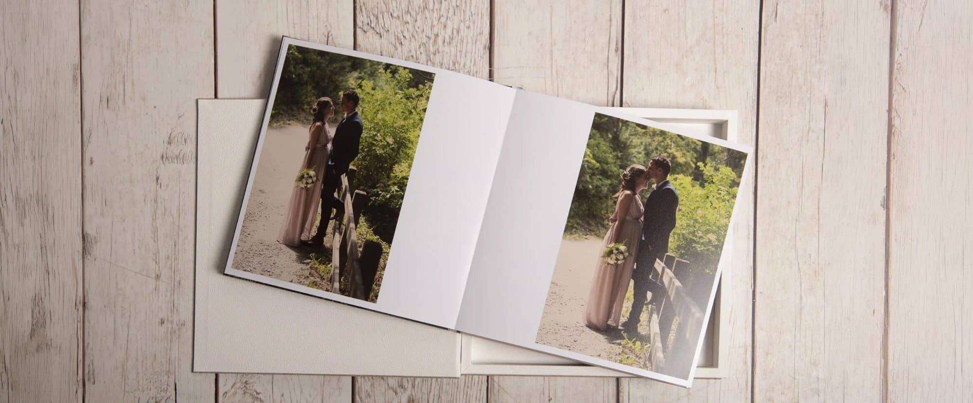 Un album de mariage ouvert sur sa boîte, posé sur des planches de bois blanchies