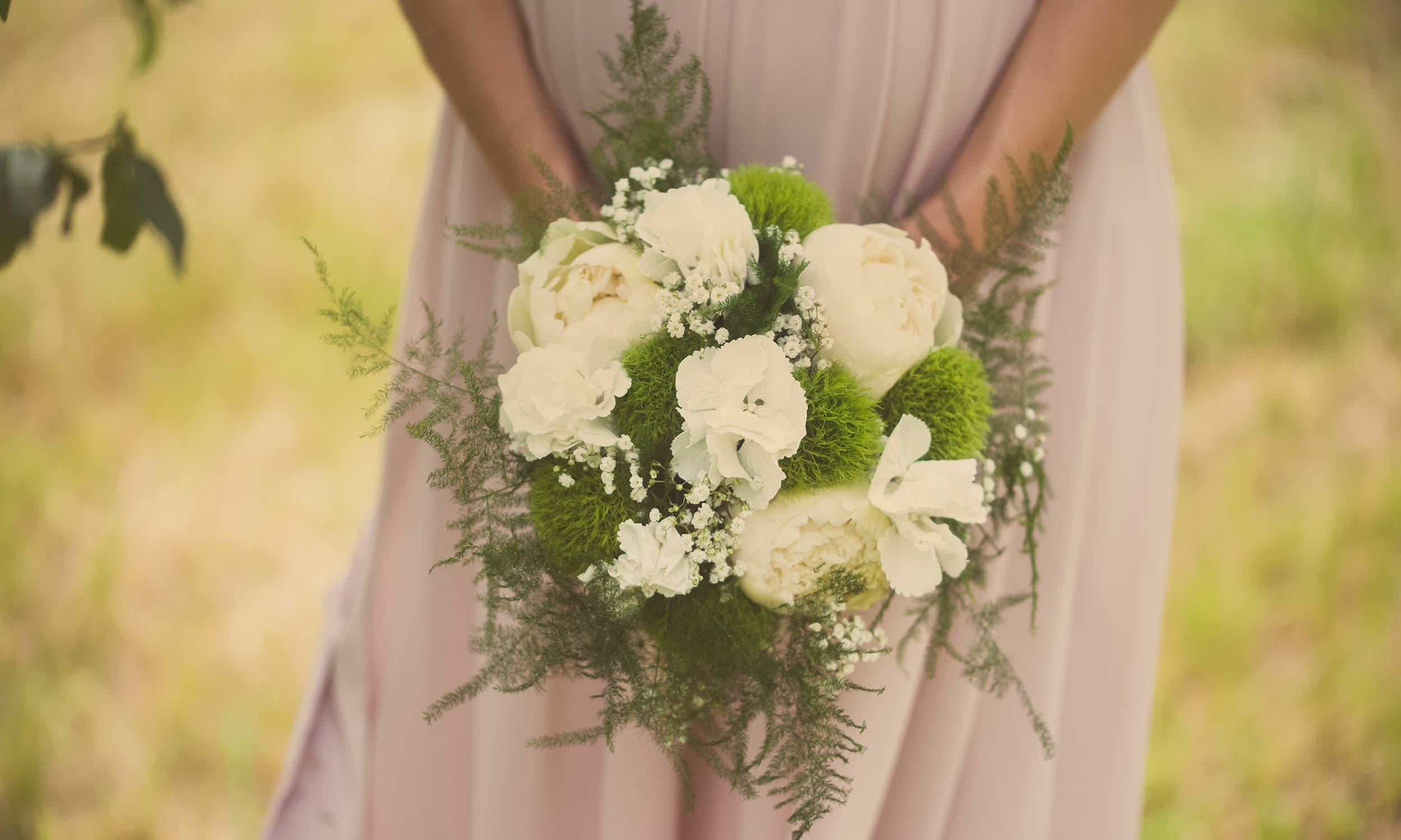 Un bouquet de fleurs blanches et de fougères tenu devant une robe rose poudré