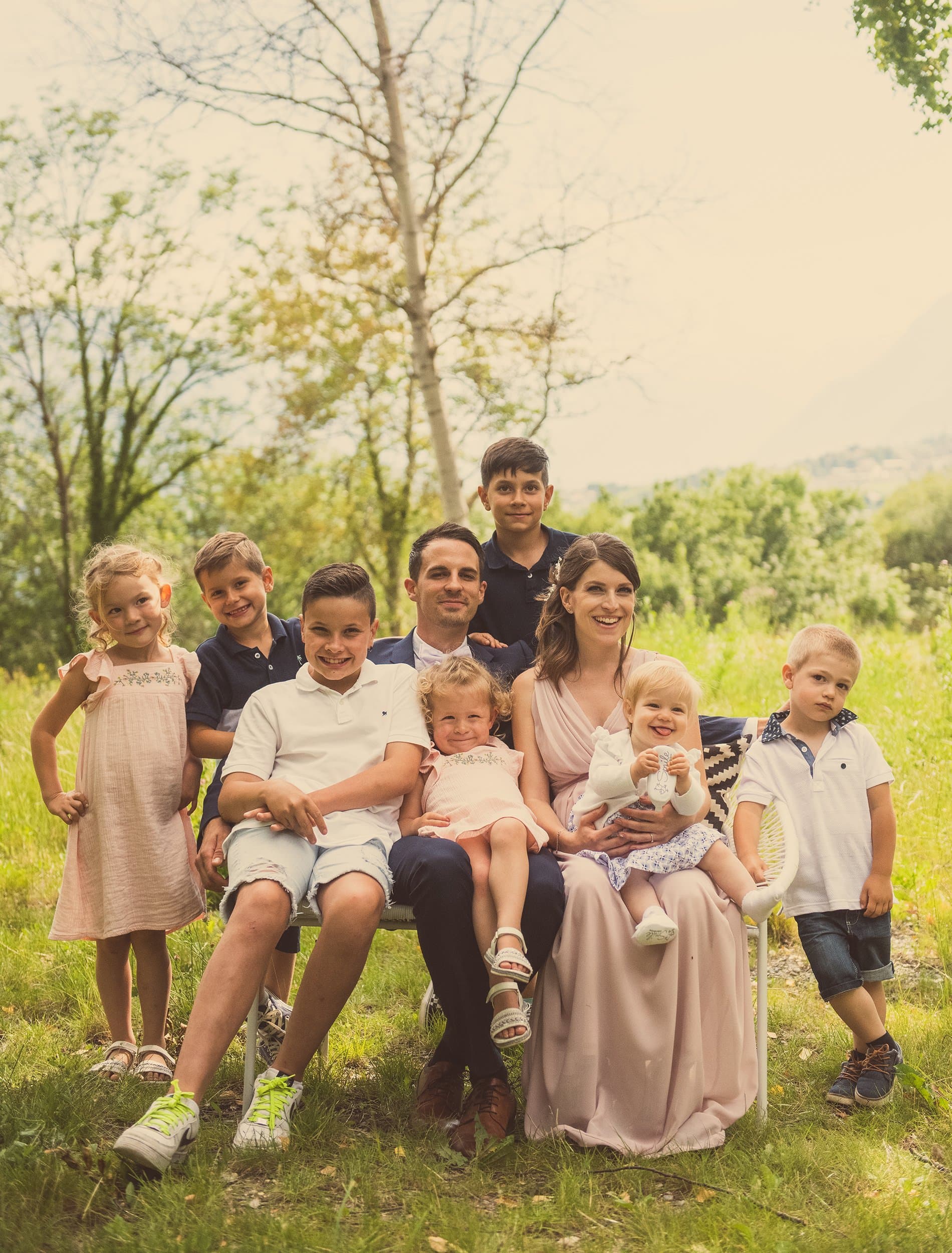 Une famille et ses sept enfants réunis sur un banc dans un pré, en tons doux
