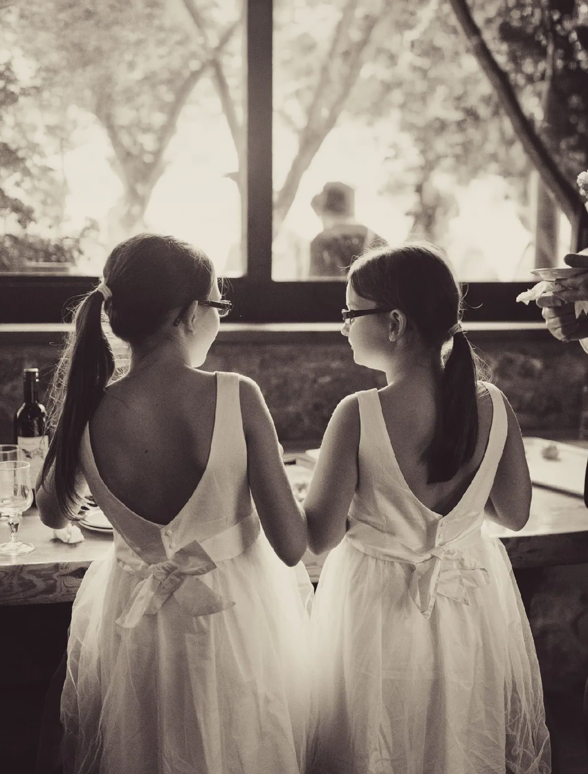 Deux fillettes en robes blanches, vues de dos, regardent la salle de fête, en tons sépia