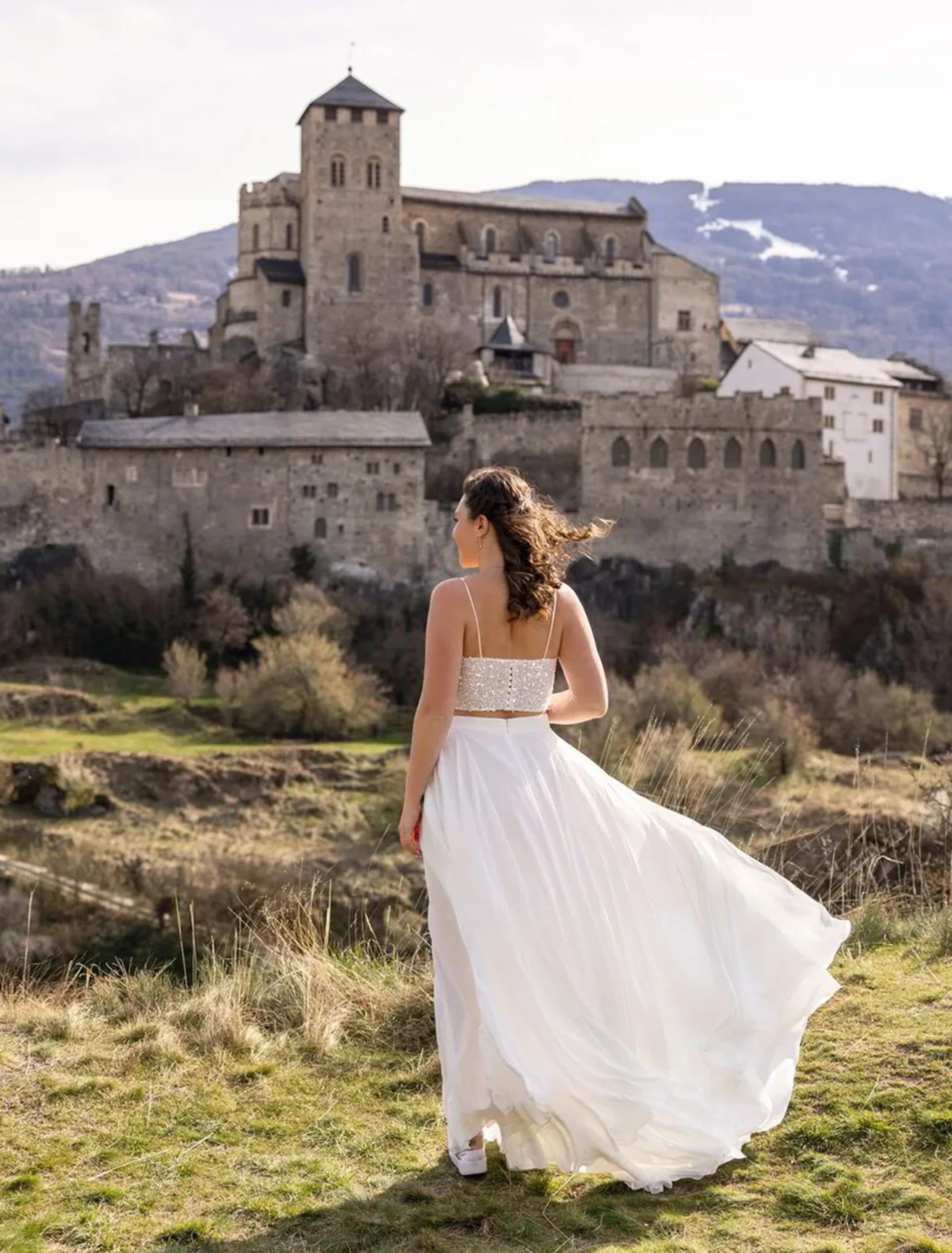 La mariée vue de dos, sa robe soulevée par le vent, face à la colline de Valère à Sion