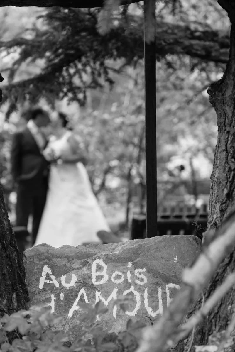 Les mariés s’embrassent derrière une pierre peinte « Au bois d’amour », en noir et blanc