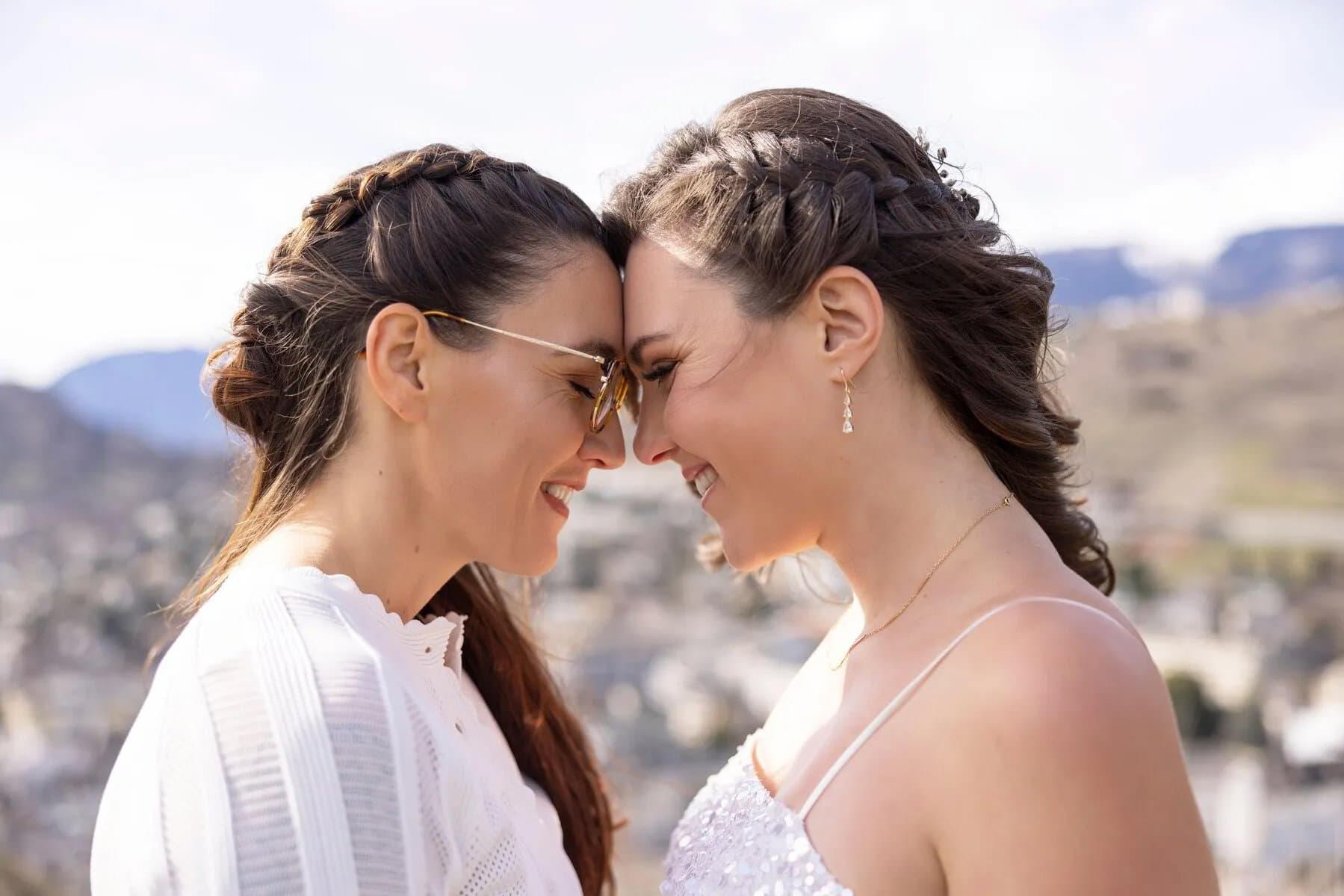 Deux mariées front contre front, la ville et les montagnes floues derrière elles