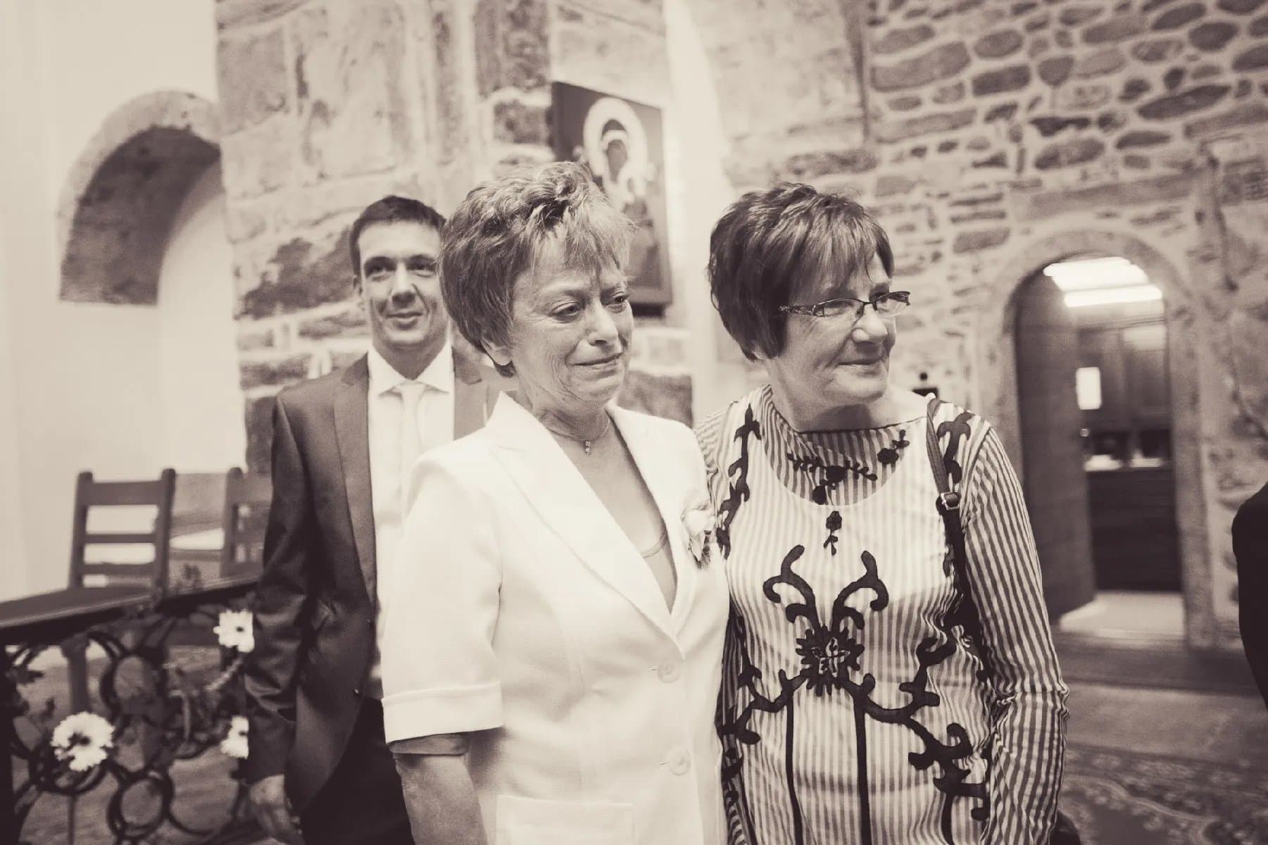 Trois invités sourient devant un mur en pierre, en tons sépia