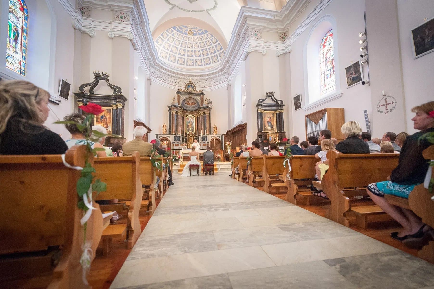 Cérémonie religieuse dans une église claire, vue depuis le fond de l’allée