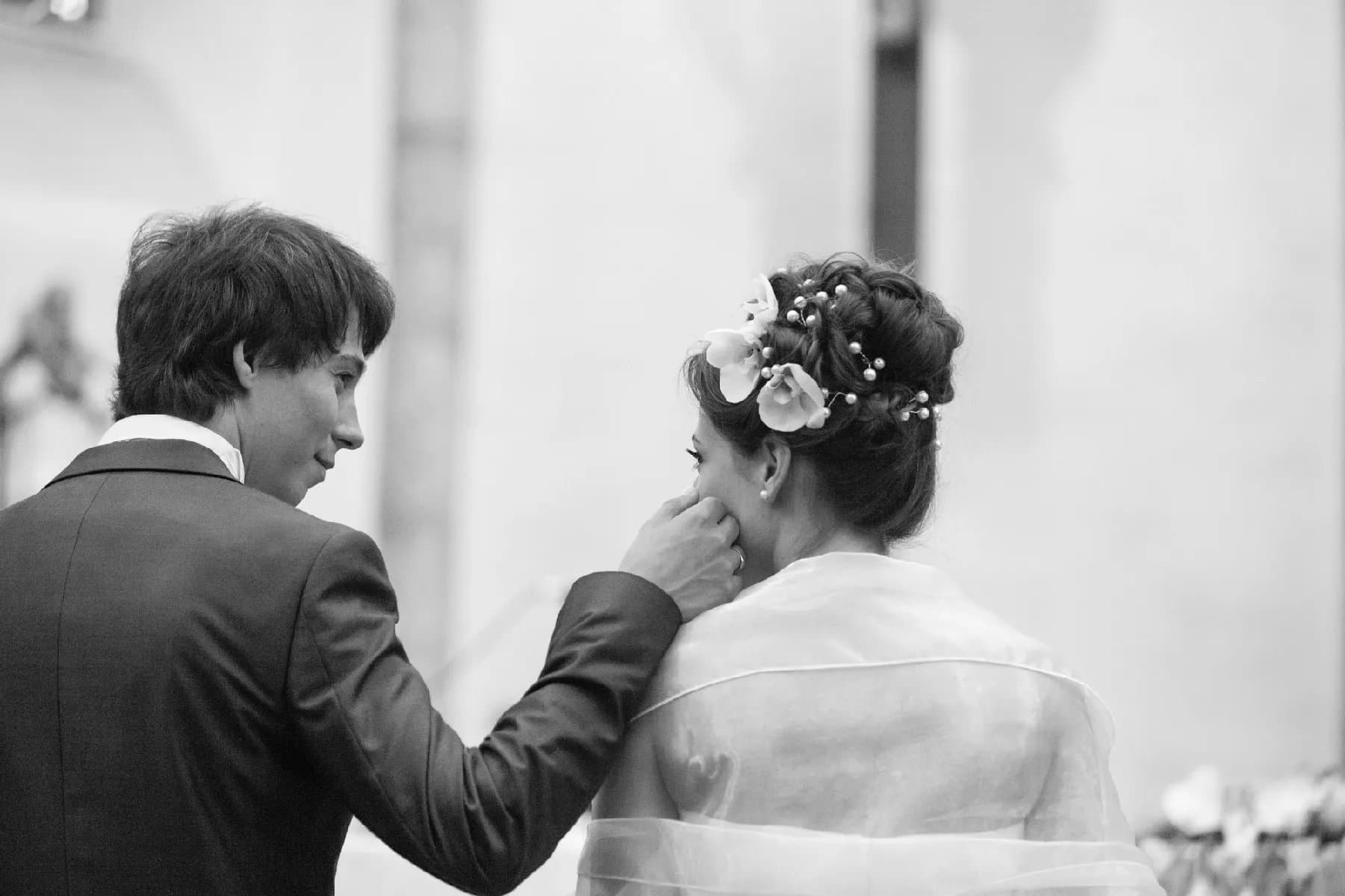Le marié caresse la joue de la mariée, en noir et blanc