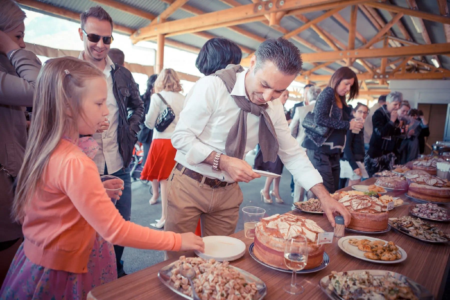 Apéritif sous un couvert en bois : une fillette et des invités se servent au buffet de tartes