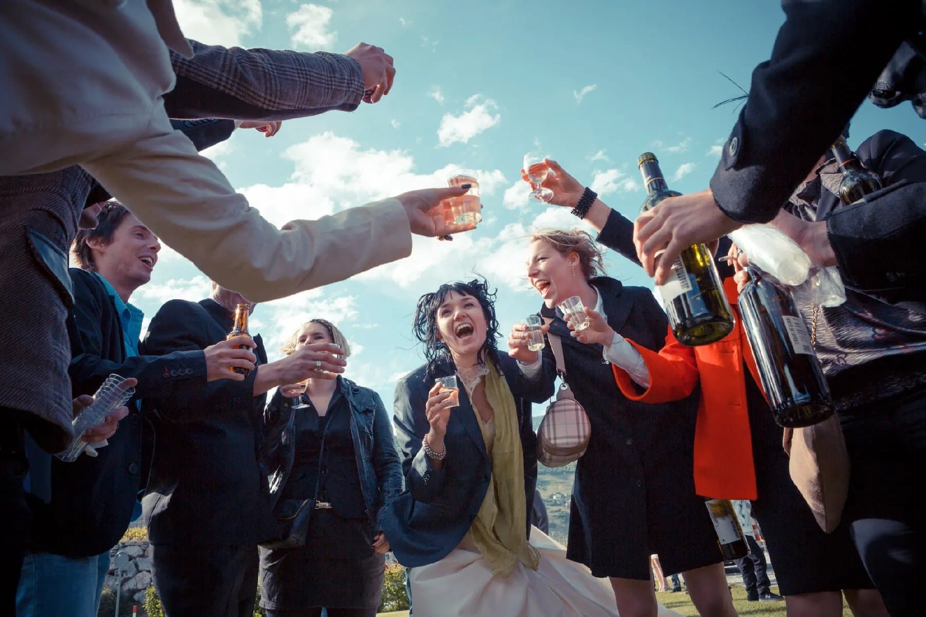 Les invités trinquent autour de la mariée, vus d’en bas sur fond de ciel bleu