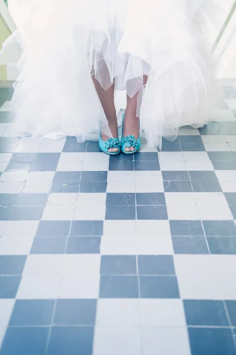 Les chaussures turquoise de la mariée sous sa robe, sur un carrelage en damier