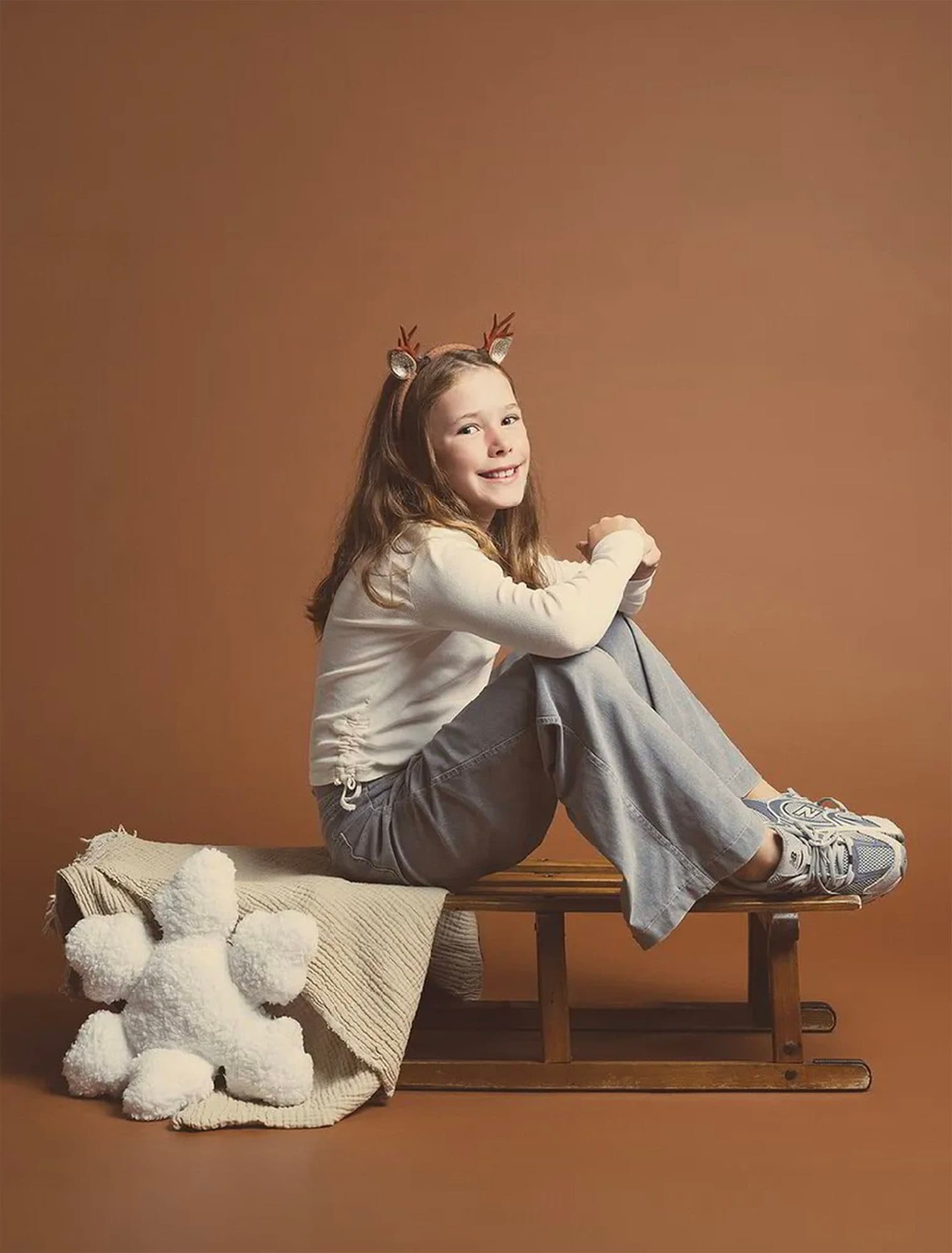 Décor Brun Cacao : une fillette coiffée de bois de renne assise sur une luge en bois, un ours en peluche blanc à ses pieds