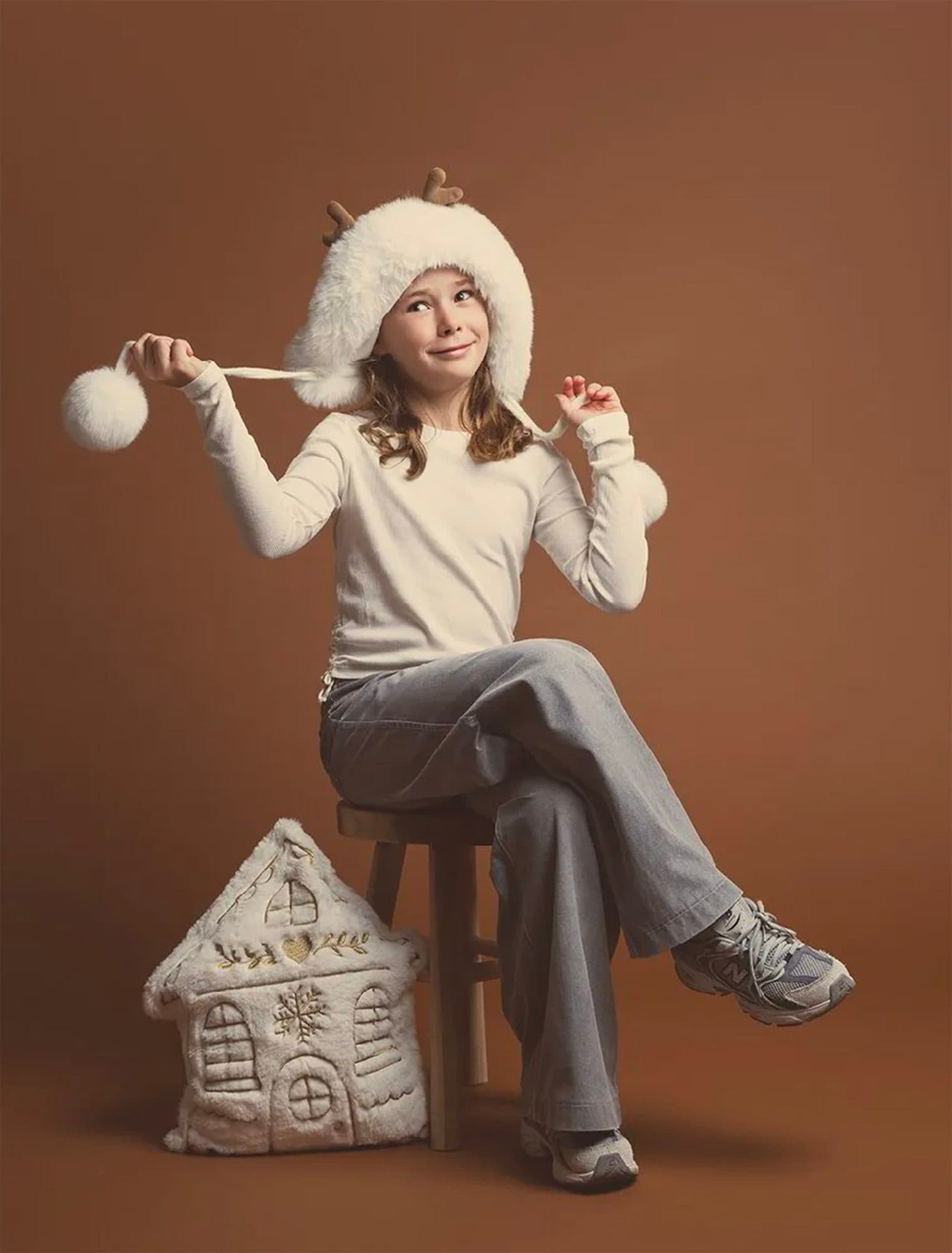 Décor Brun Cacao : une fillette en bonnet blanc à pompon assise sur un tabouret, une maison en tissu à ses pieds
