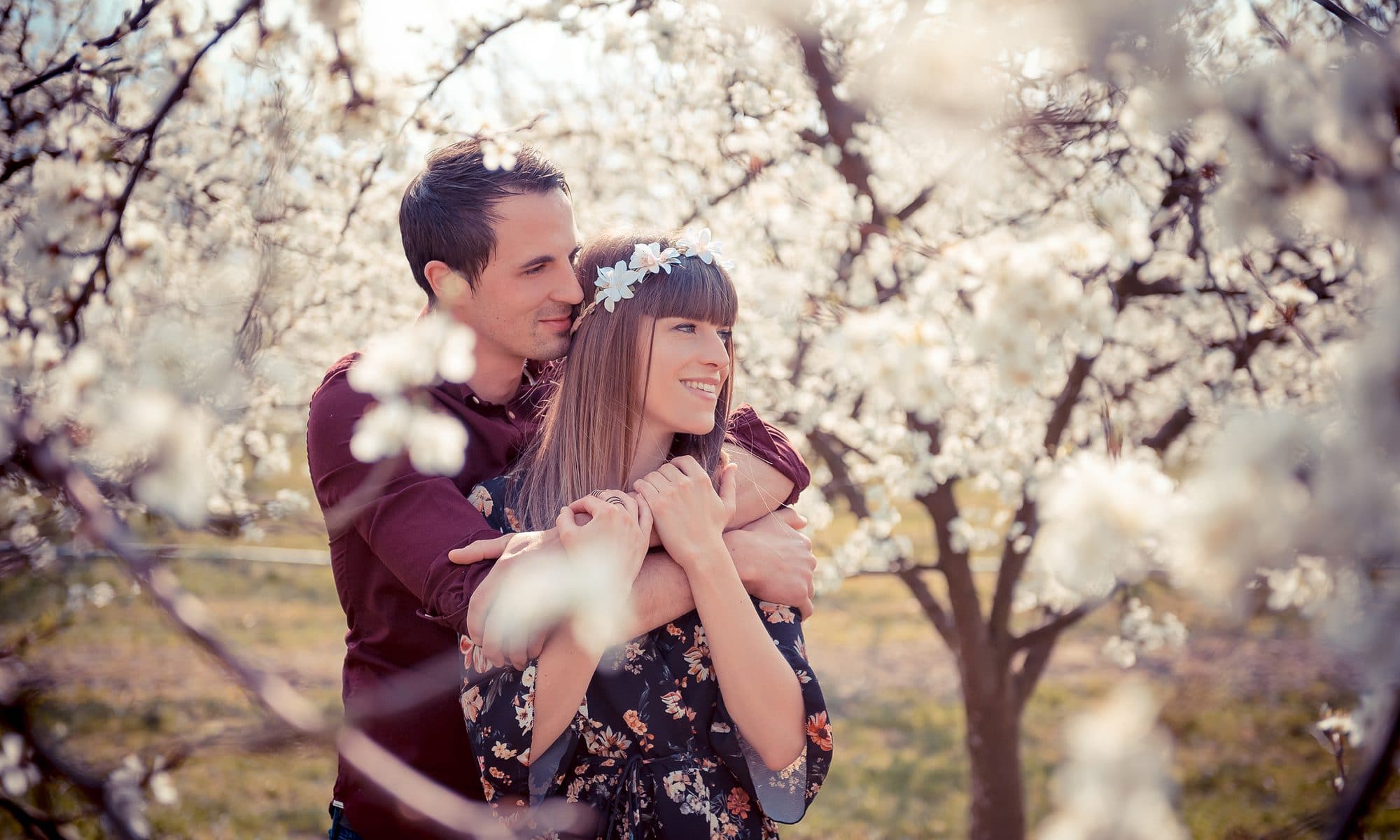 Un couple enlacé et souriant sous les branches d’un cerisier en fleurs