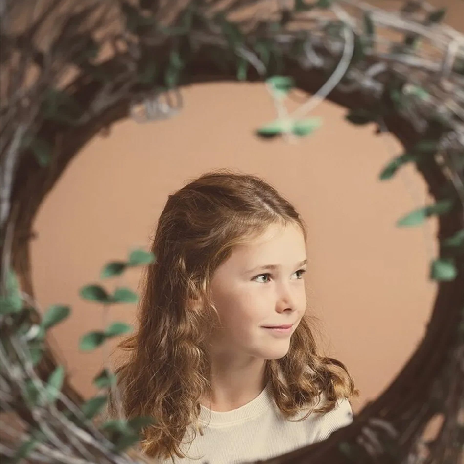 Le portrait d’une fillette aux cheveux bouclés, encadré d’une couronne de branchages
