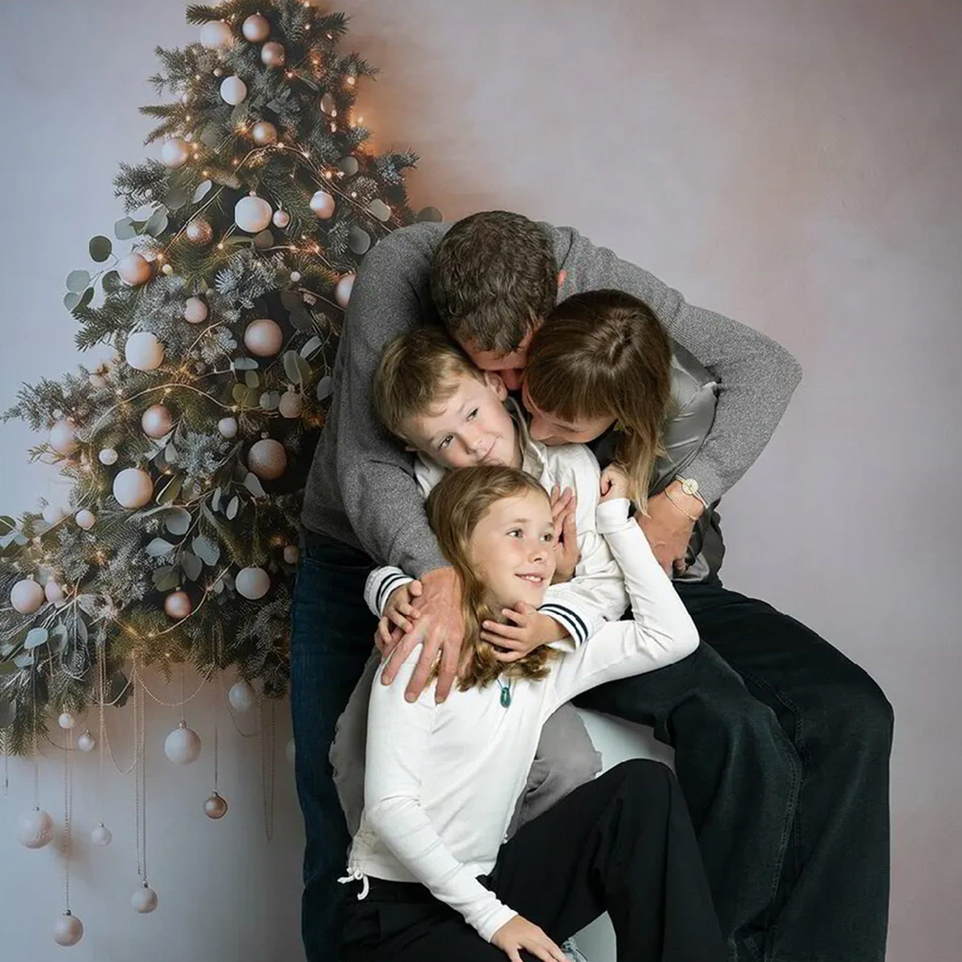 Une famille enlacée devant un sapin de Noël, assise sur un cube blanc