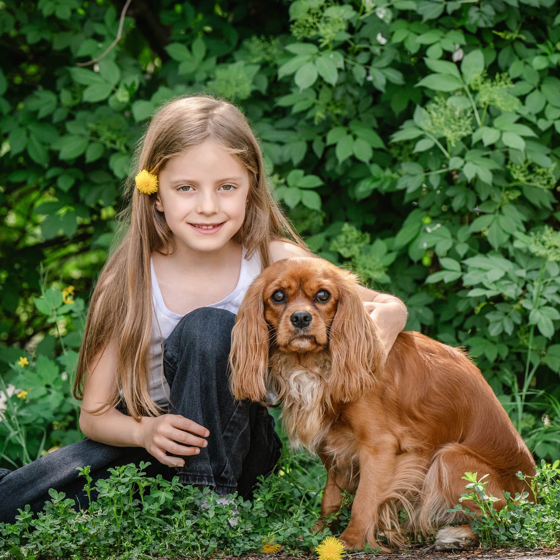 Une fillette, une fleur jaune dans les cheveux, enlace son chien dans la verdure