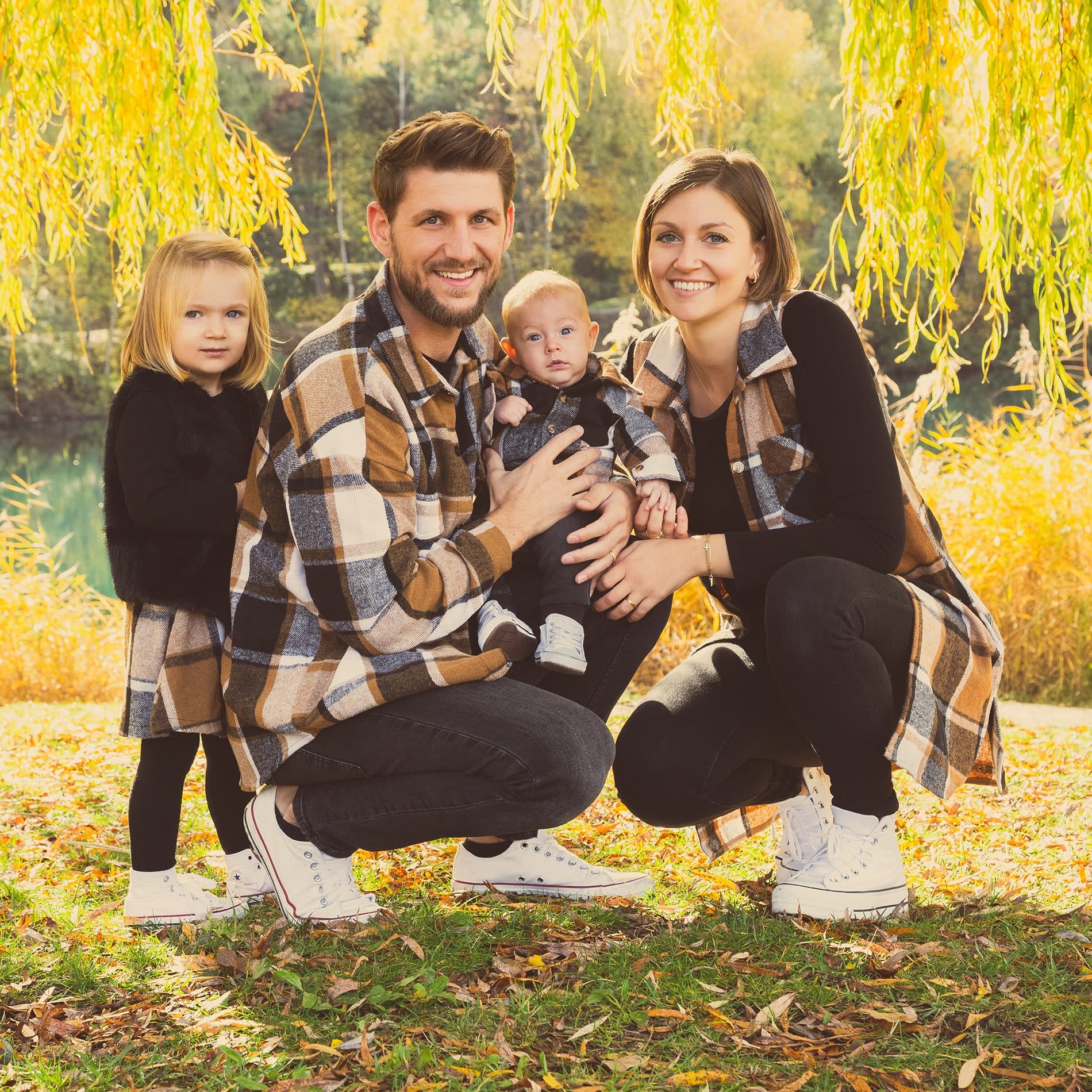 Une famille accroupie dans les feuilles d’automne, en chemises à carreaux