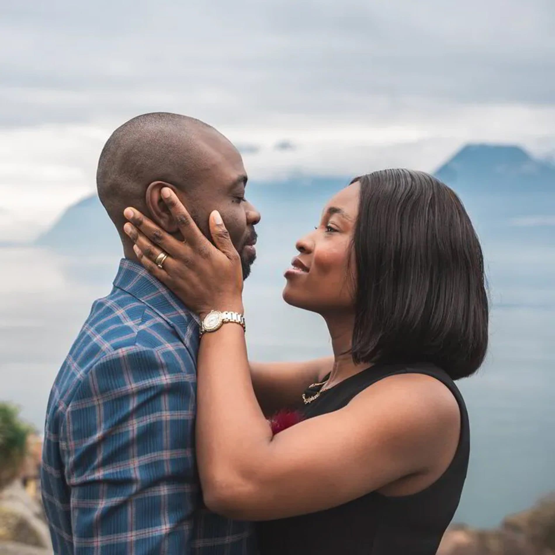 Un couple face à face, la main sur la joue, devant un lac et les montagnes