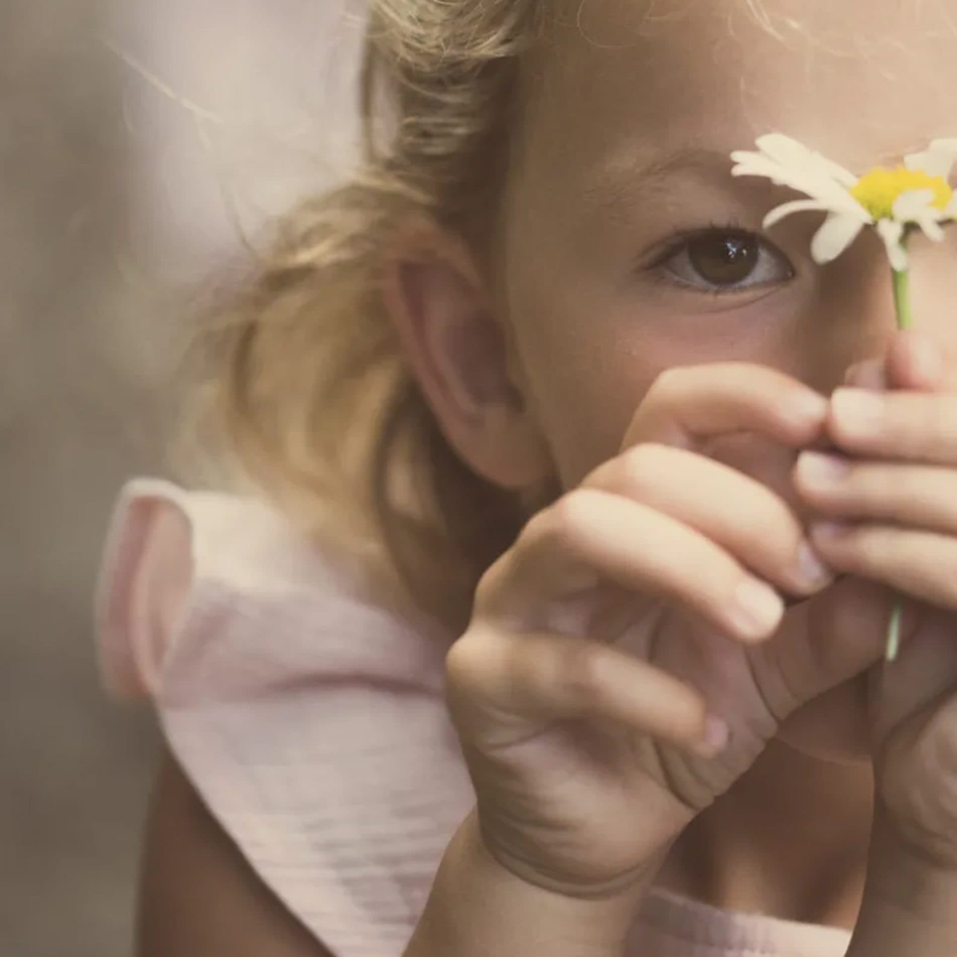 Une fillette cache un œil derrière une marguerite, dans une lumière douce