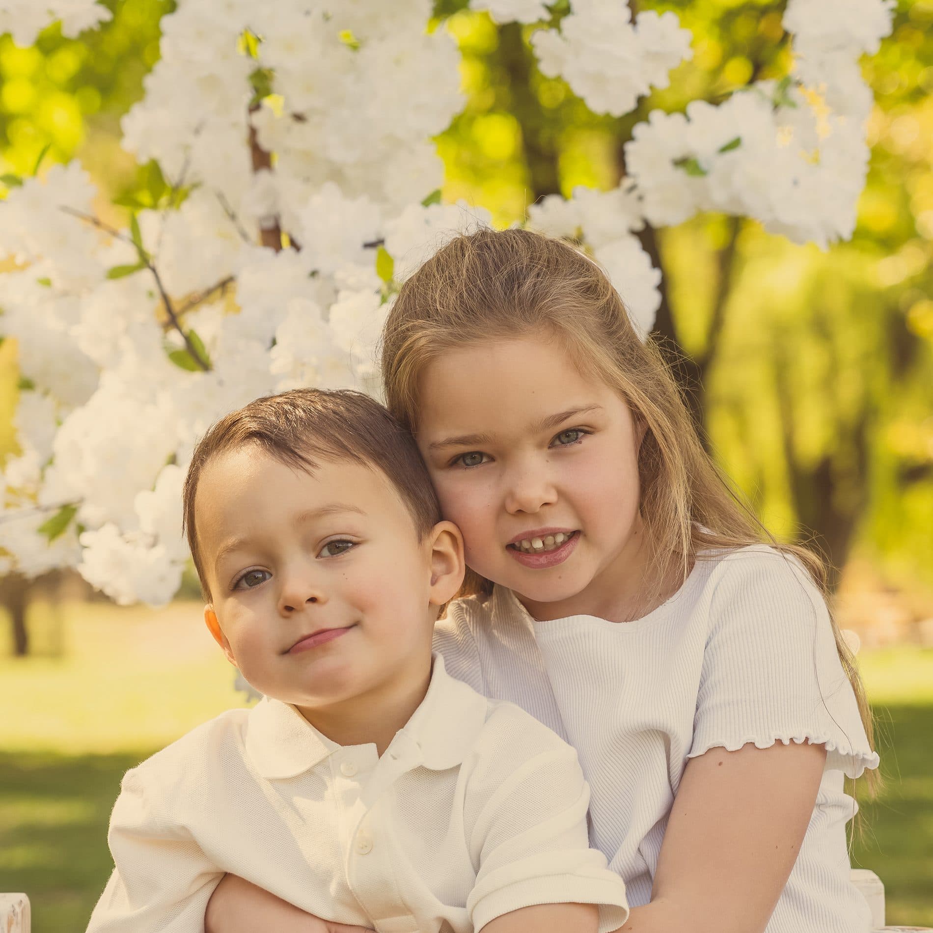 Un frère et sa sœur joue contre joue, sous des fleurs blanches