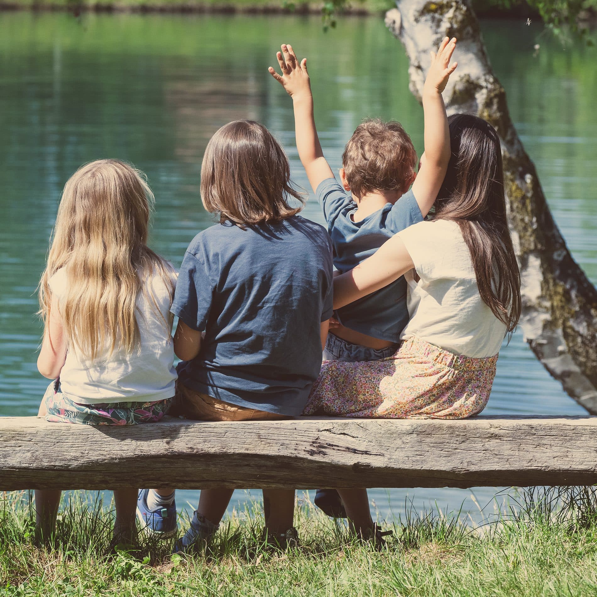 Des enfants et leur maman de dos, assis sur un banc au bord d’un étang
