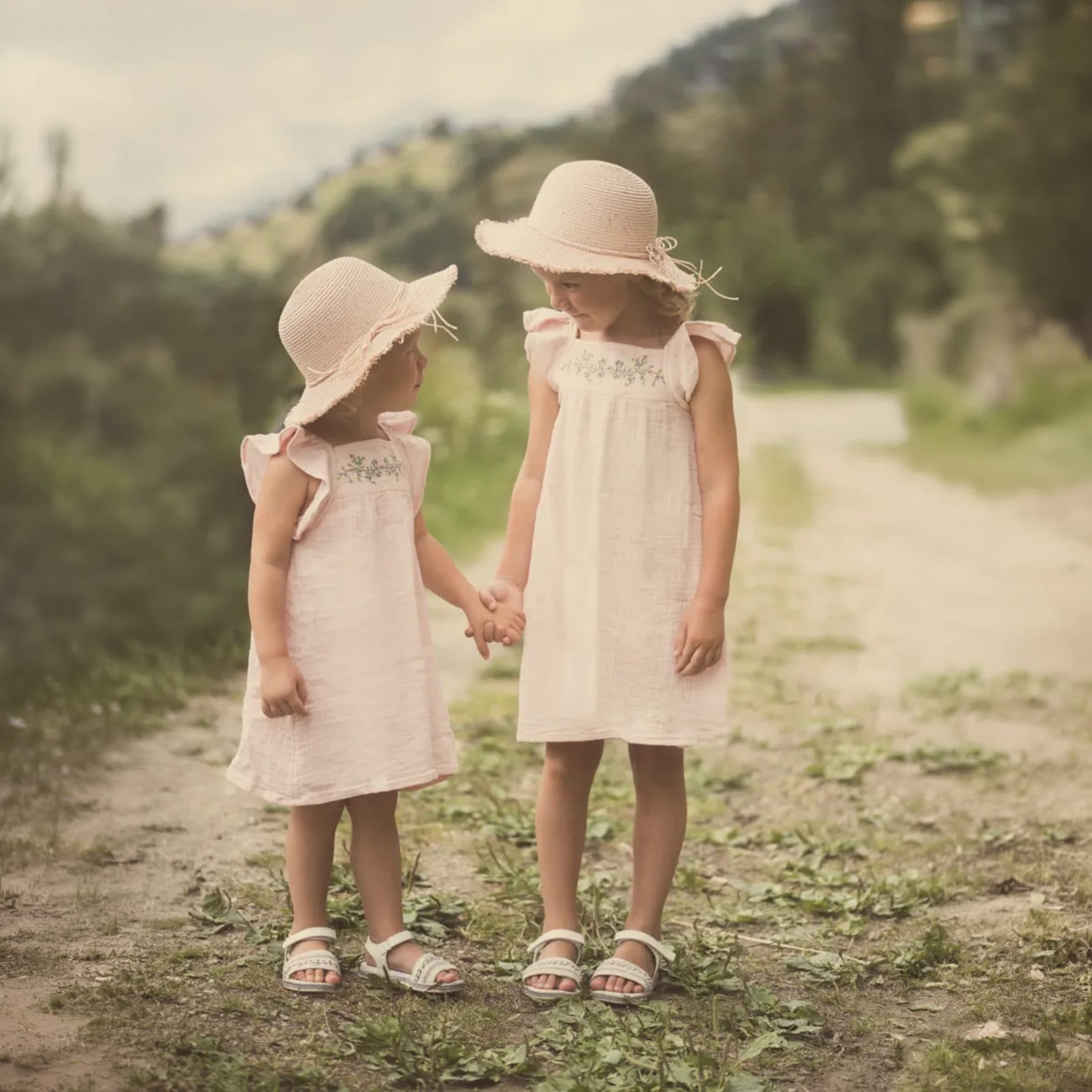 Deux petites sœurs en chapeaux de paille, main dans la main sur un chemin