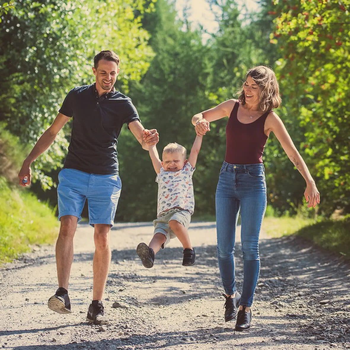 Des parents font sauter leur petit garçon en le tenant par les mains, sur un chemin