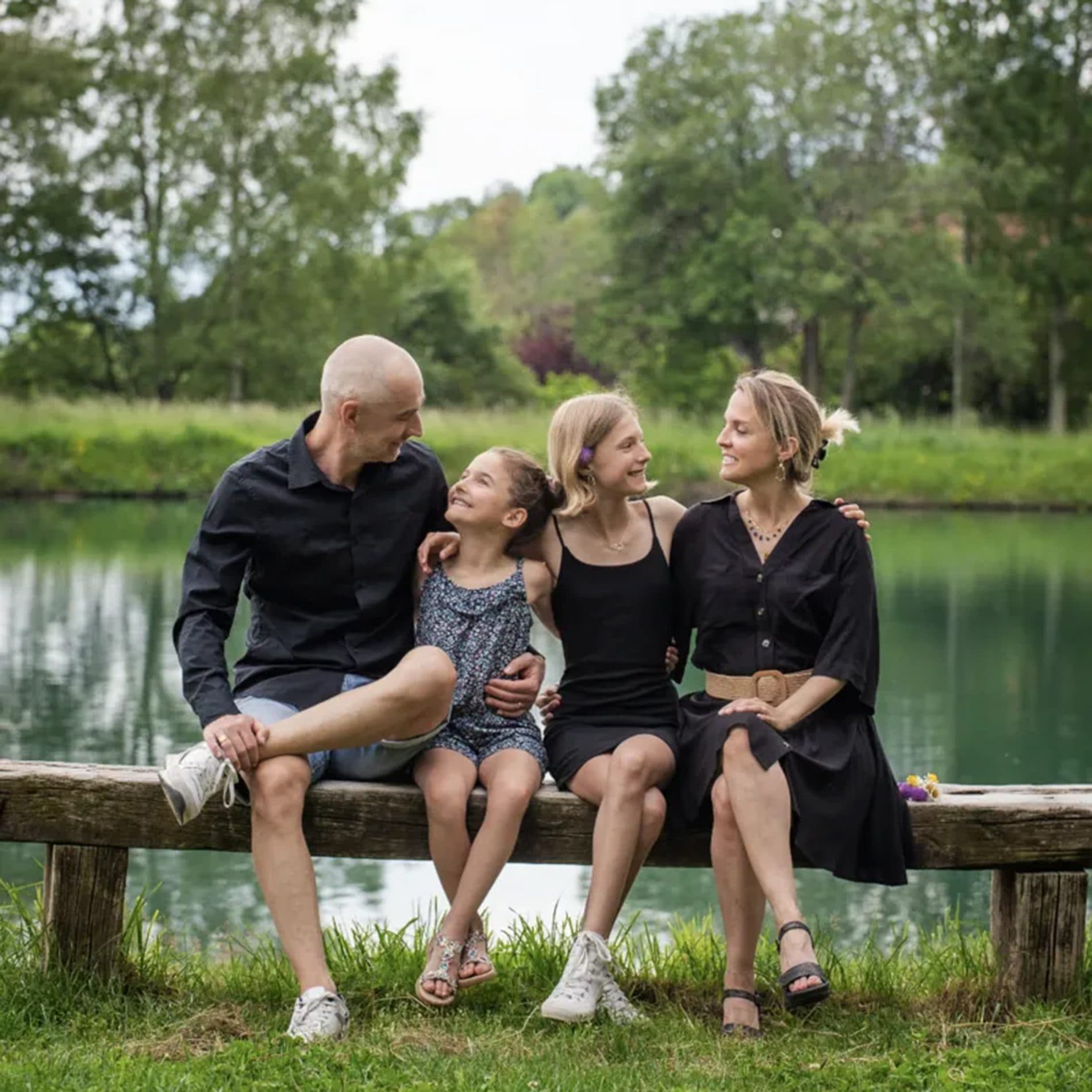 Une famille assise sur un banc au bord d’un étang