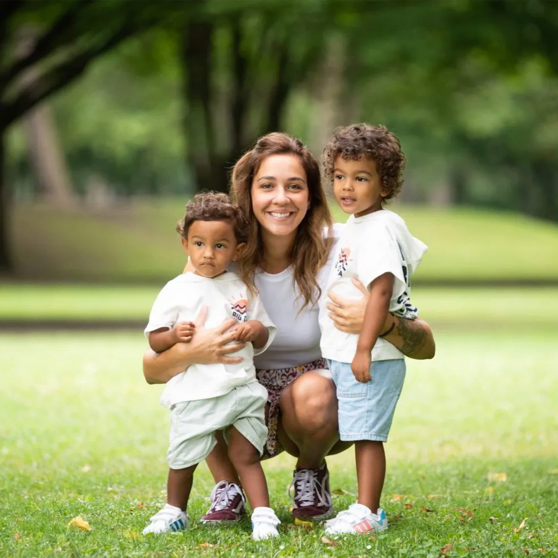 Une maman accroupie entre ses deux petits garçons, dans un parc