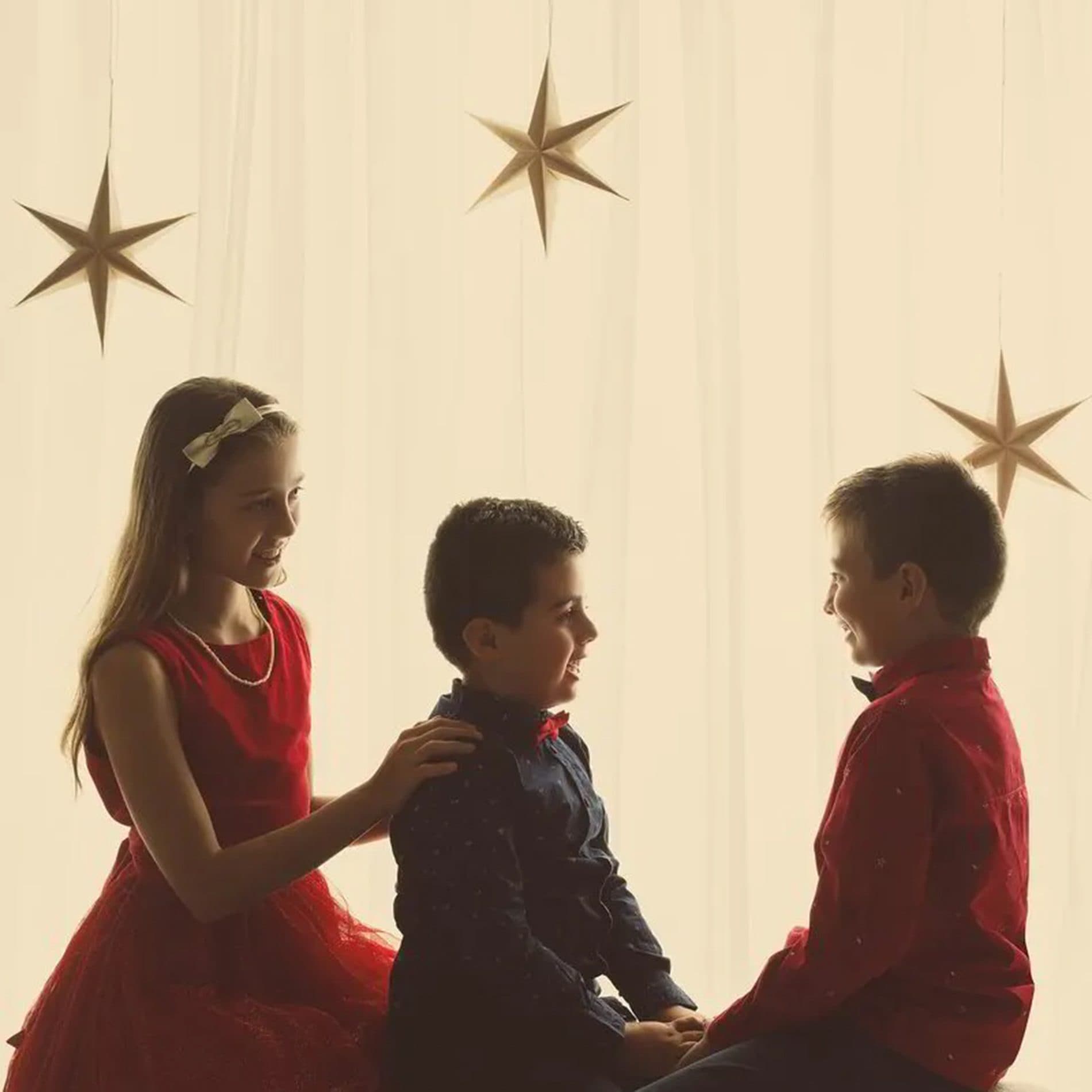 Les silhouettes de trois enfants en rouge devant un rideau crème et des étoiles