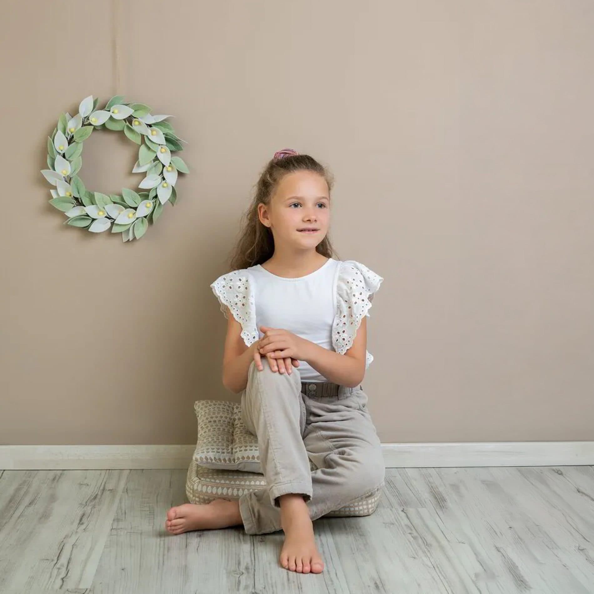 Une fillette assise sous une couronne de verdure, devant un fond beige