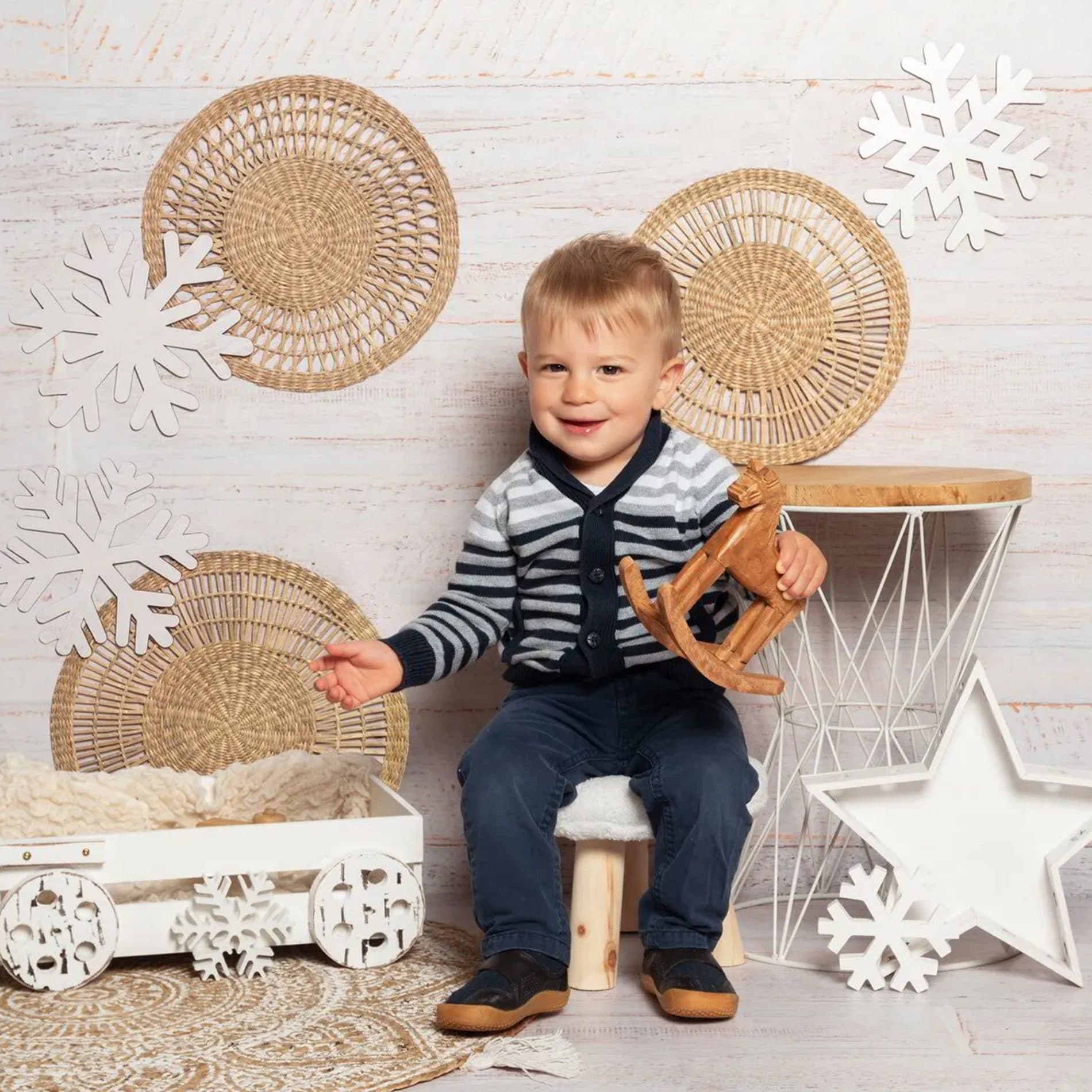 Un petit garçon en gilet rayé dans un décor d’hiver en osier, avec des flocons et une étoile blanche